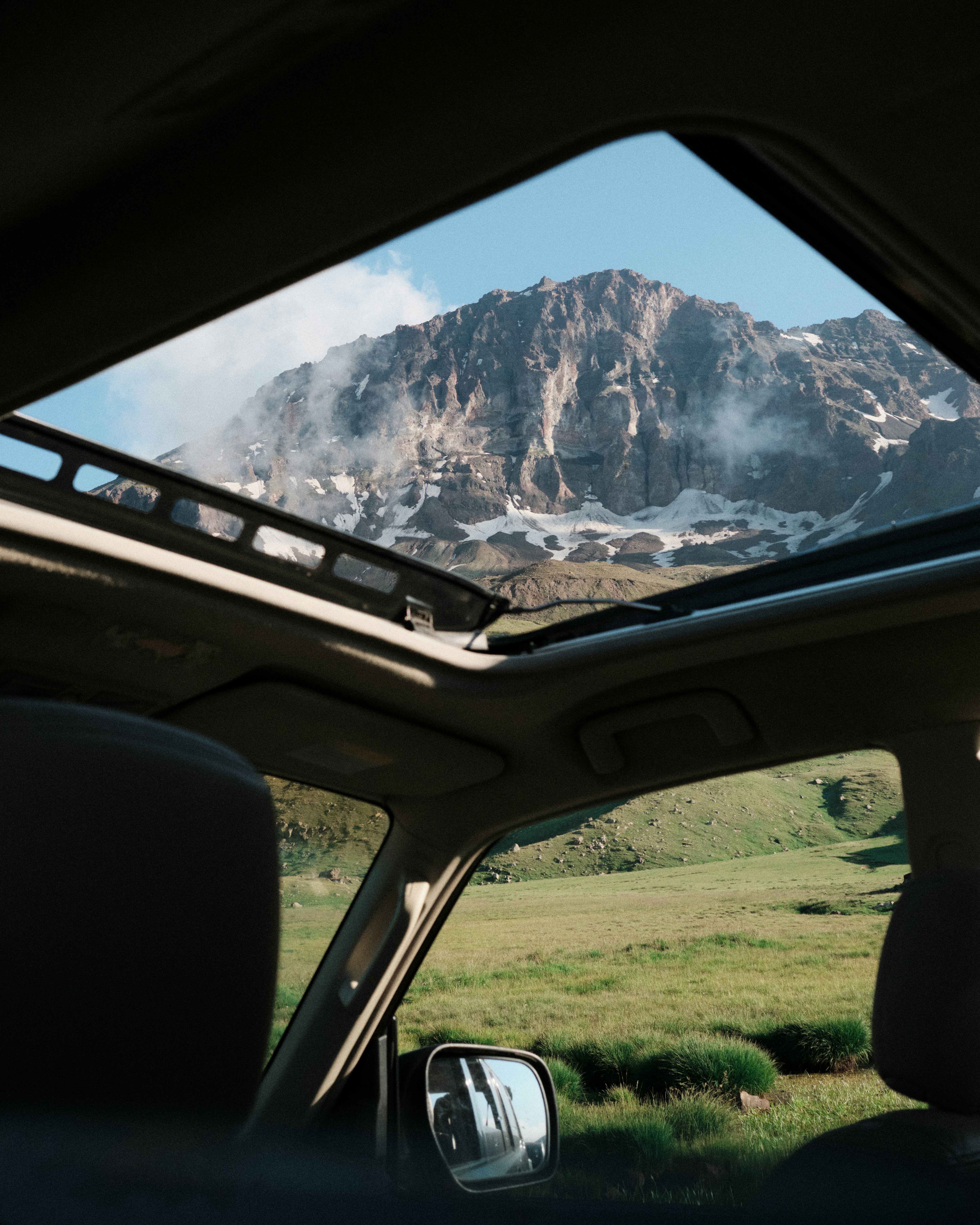 A view of a snow-capped mountain through an open car sunroof