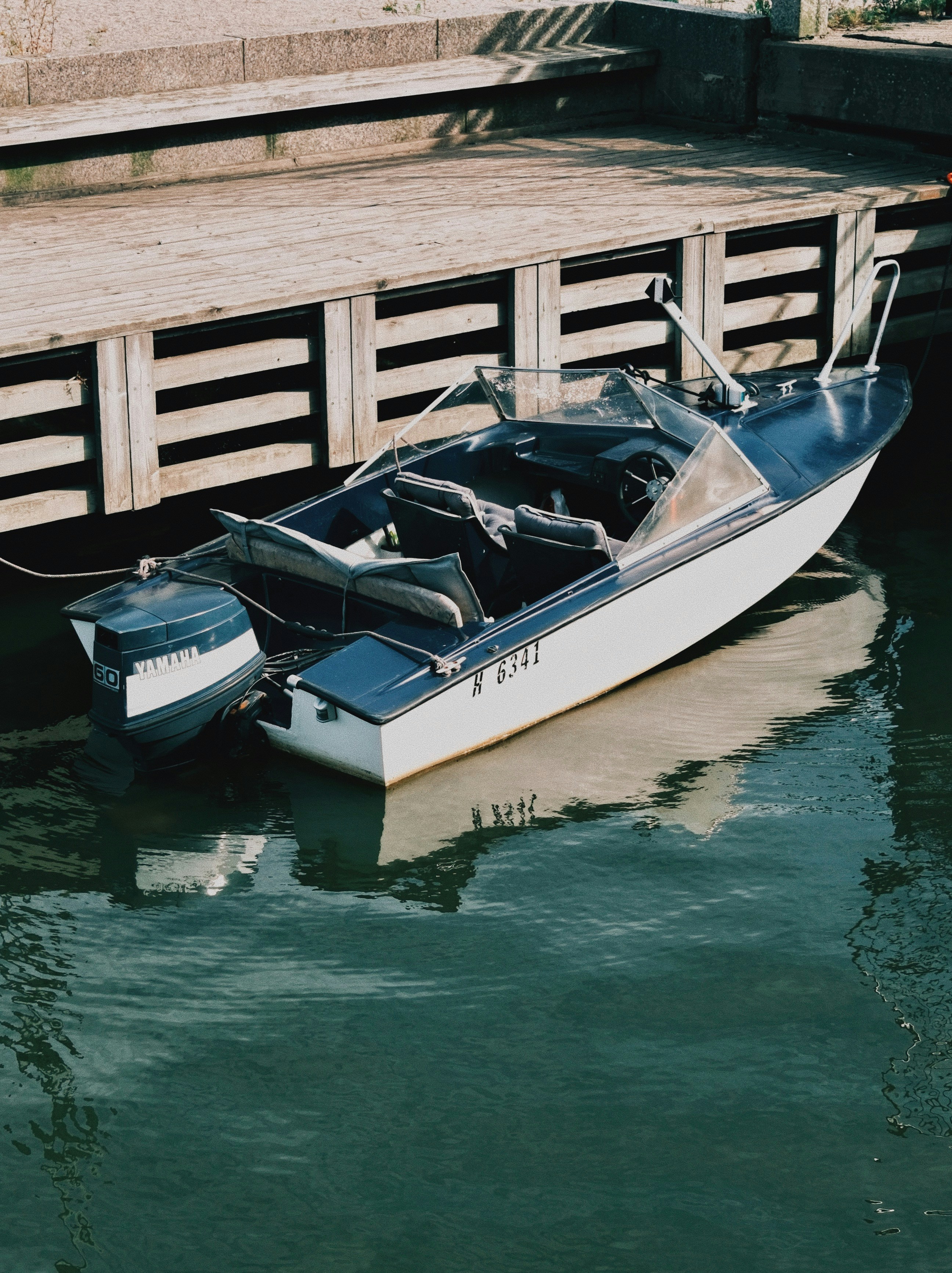 A small motorboat moored to a wooden dock on calm green water