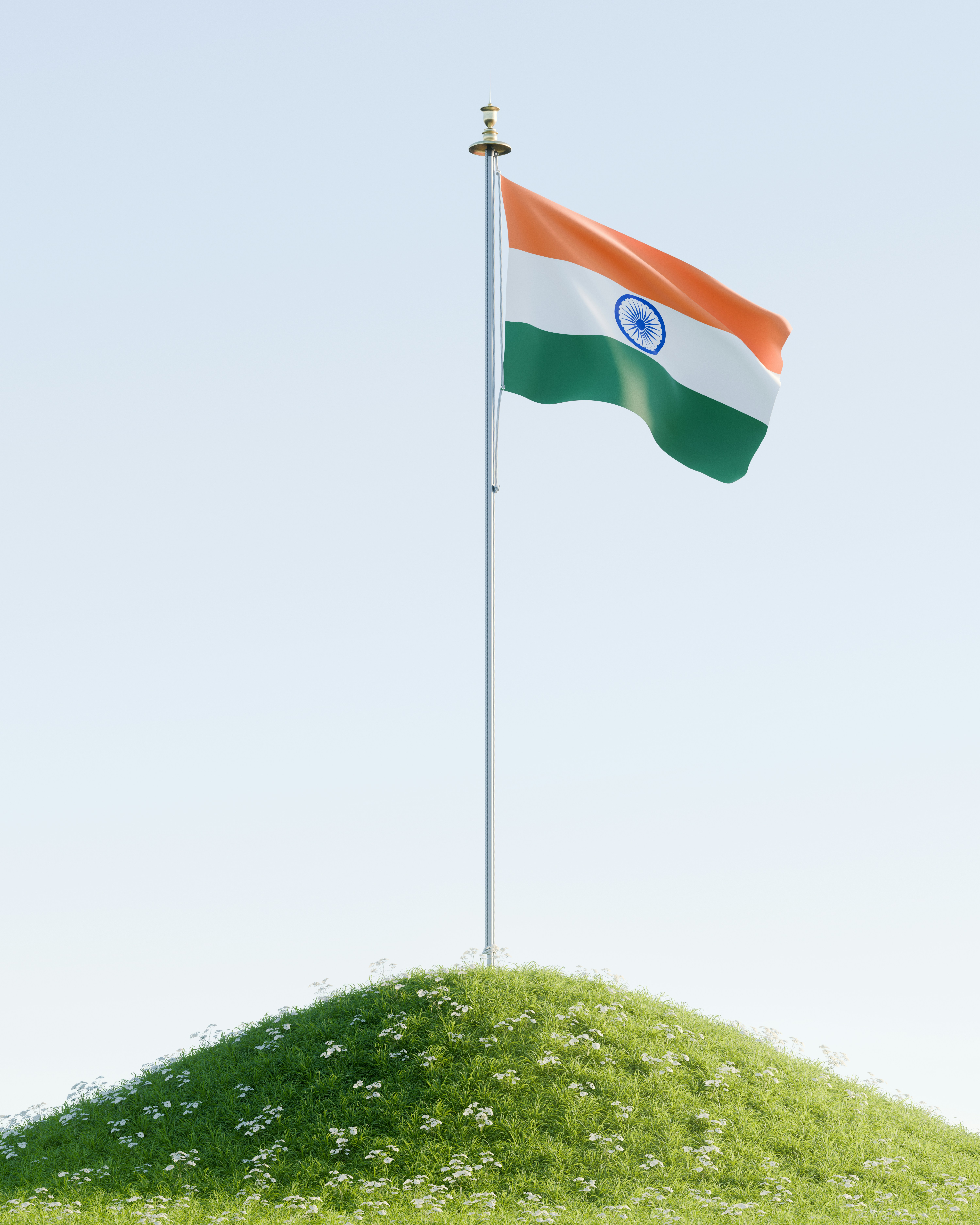 The flag of India waving on a tall pole atop a grassy hill