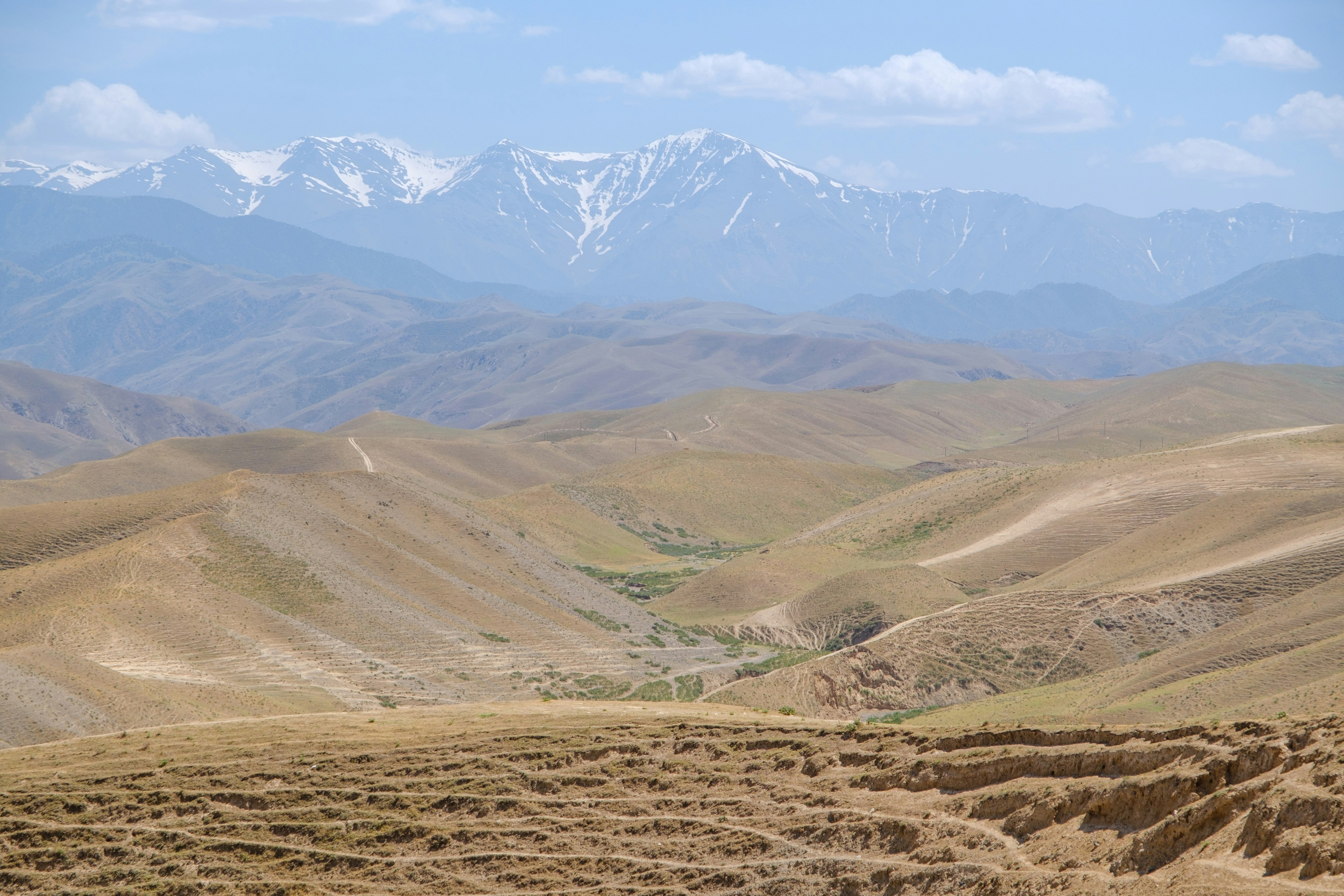 Snow-capped mountains rising above rolling brown hills under a blue sky