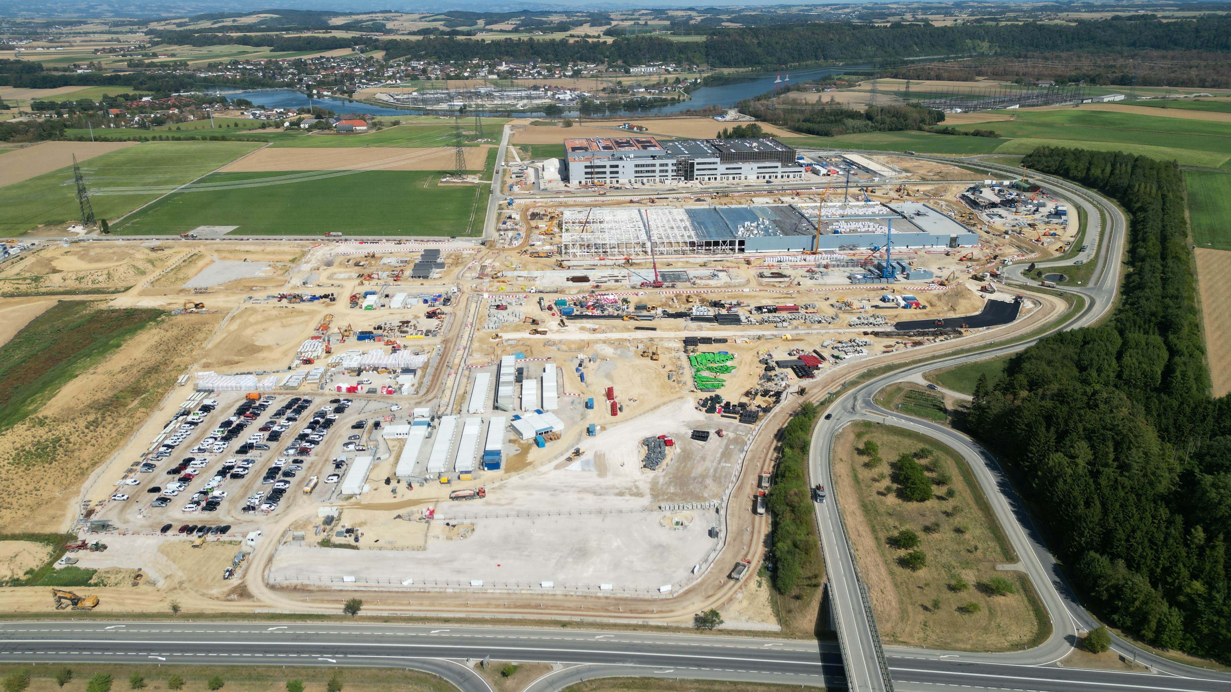 An aerial view of a large industrial construction site with parking and fields