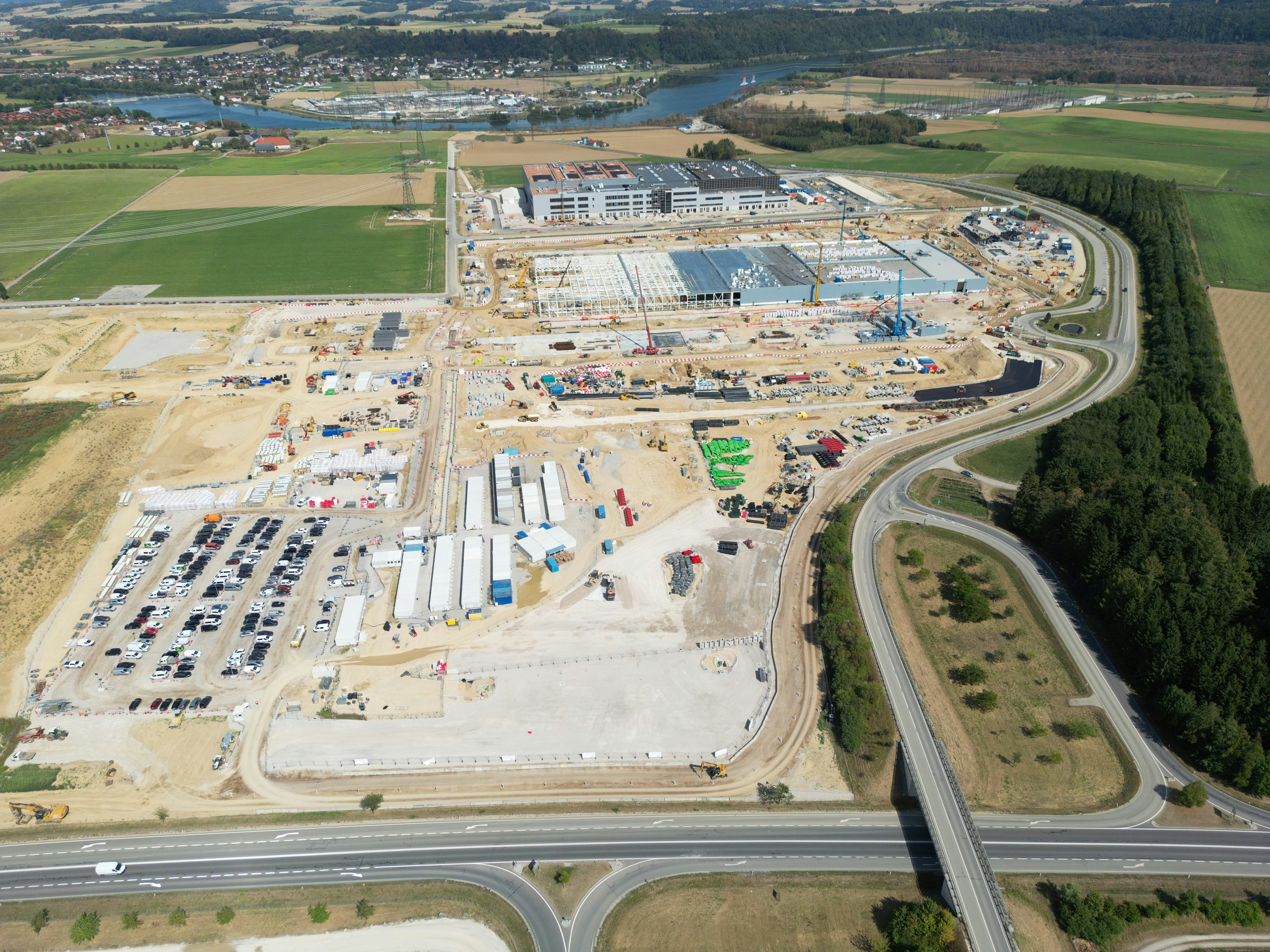 Aerial view of a large industrial construction site with parking and surrounding fields