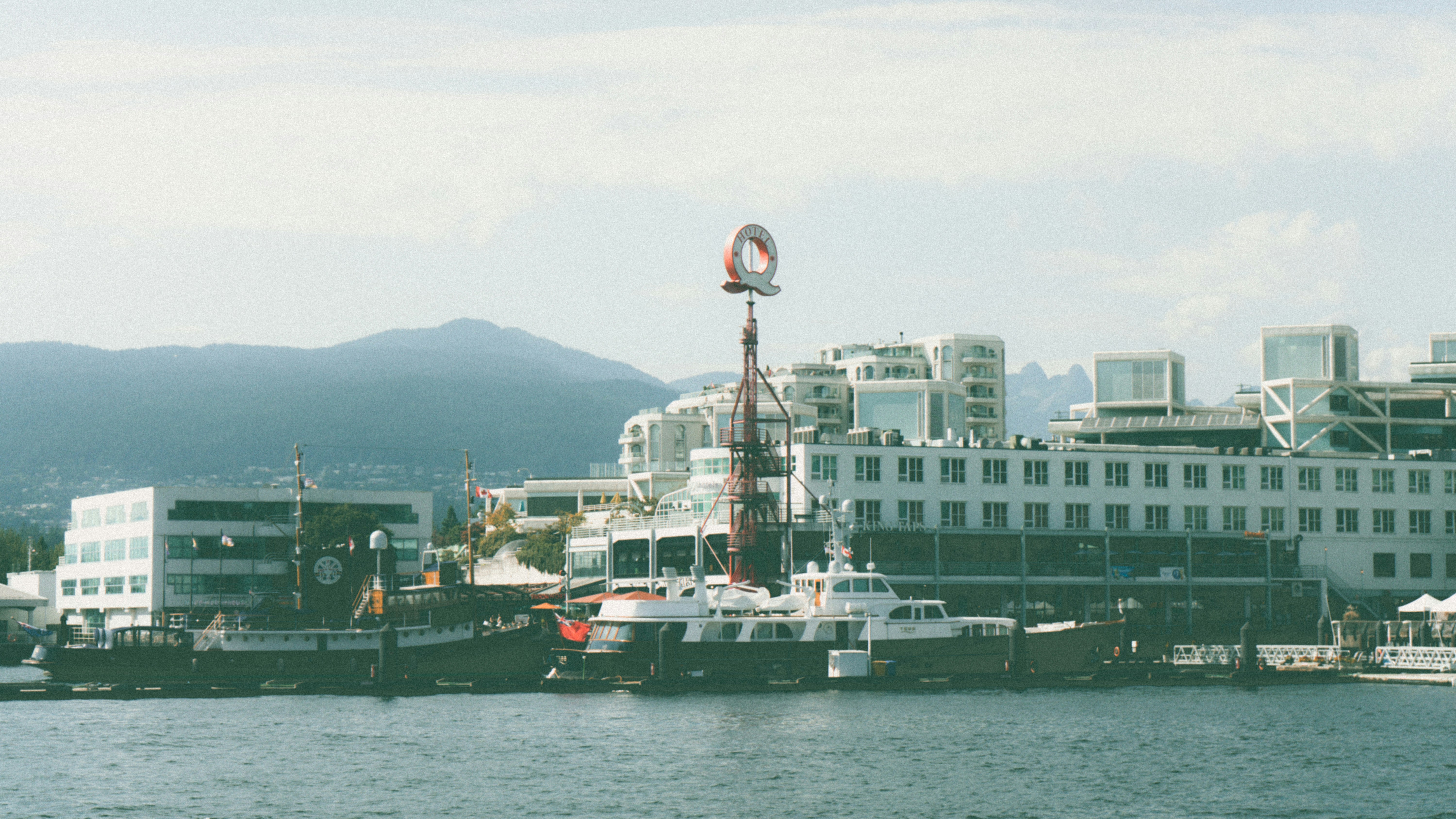 Boats moored at a waterfront with a large red Q sign in Vancouver