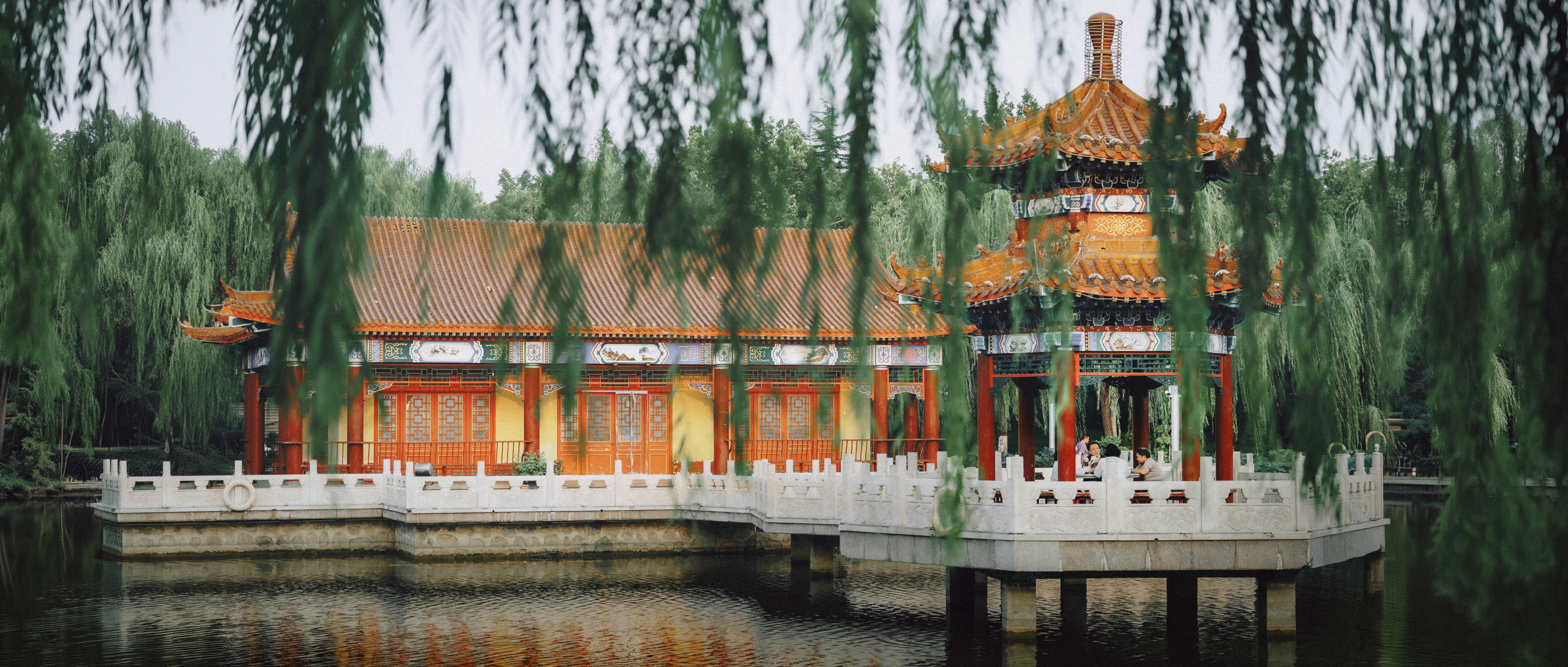 Traditional Chinese pavilion and building on a lake framed by weeping willow branches