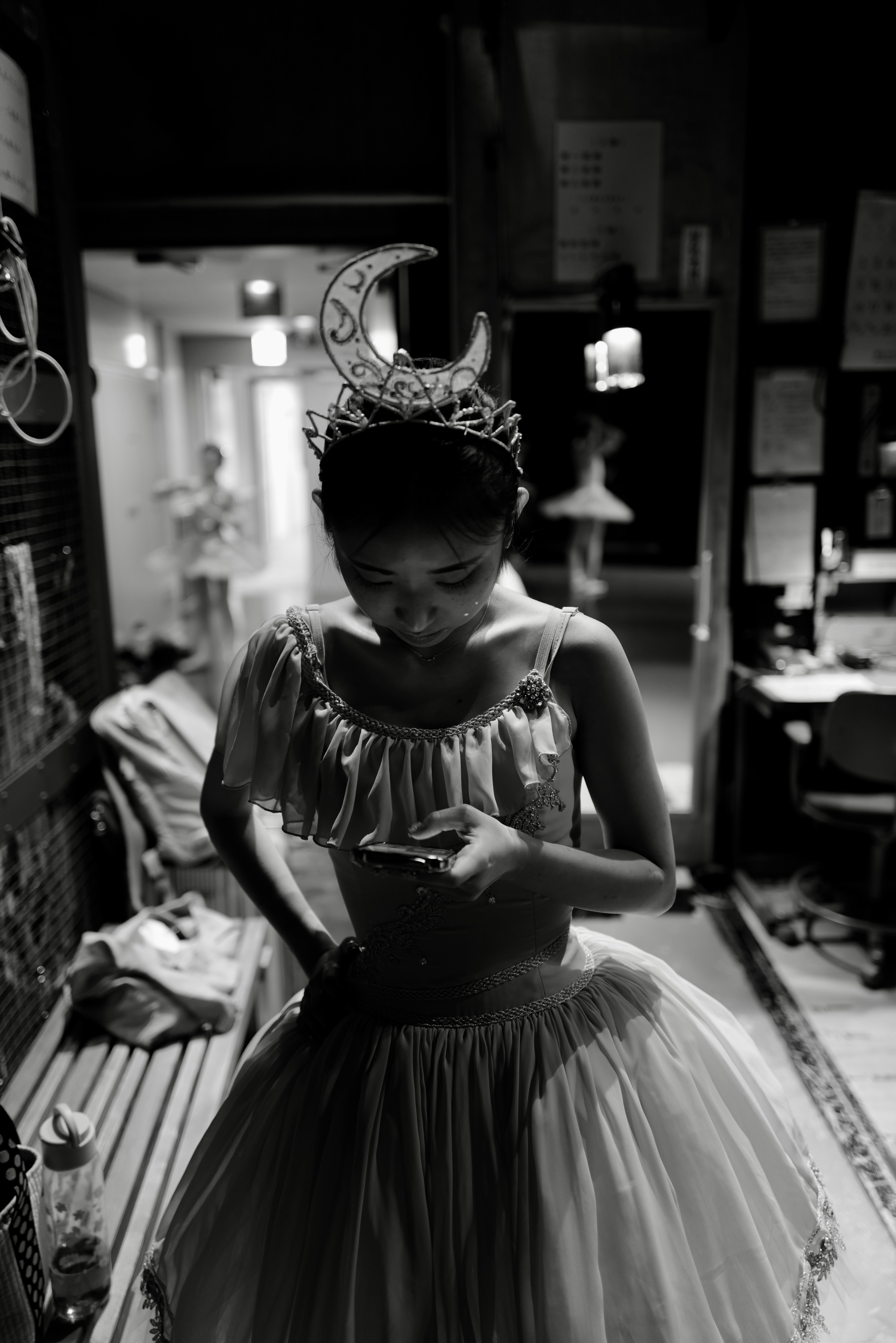 A ballerina in a crescent moon headpiece looking at a phone in a dressing room