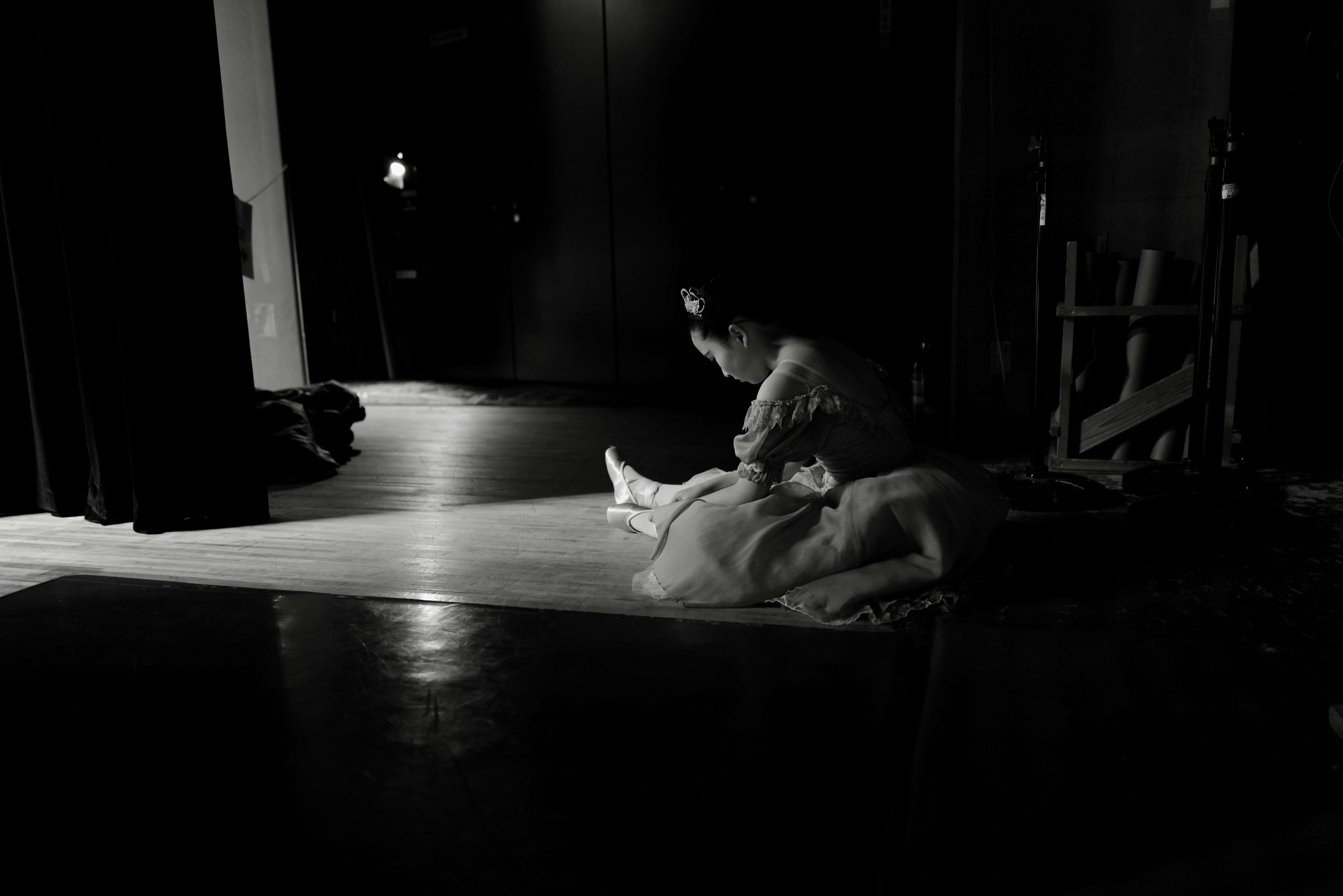 A ballerina in a tutu sitting on a stage in a pool of light