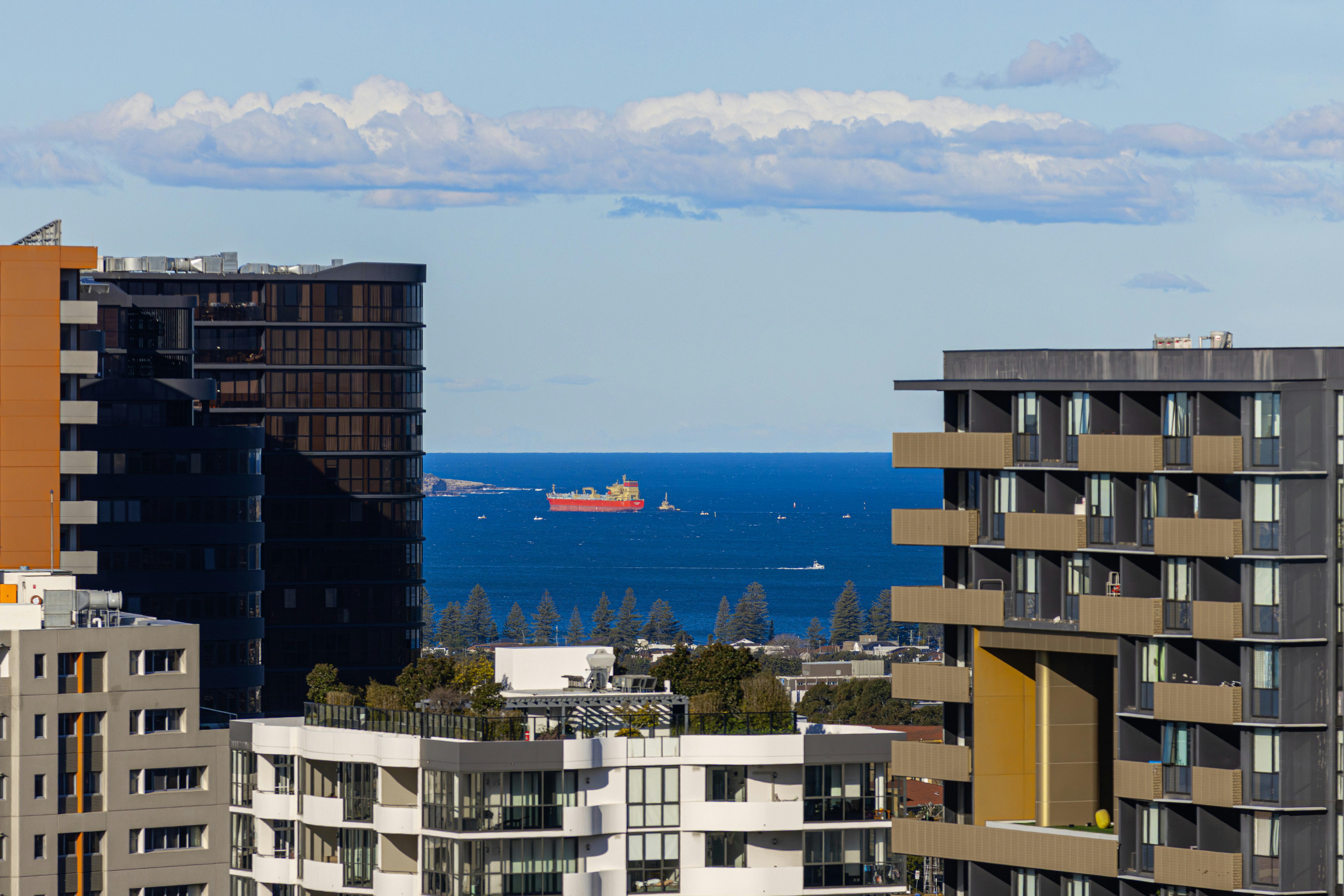 Modern apartment buildings in Sydney overlooking the Pacific Ocean, with a cargo ship visible offshore and a clear blue 