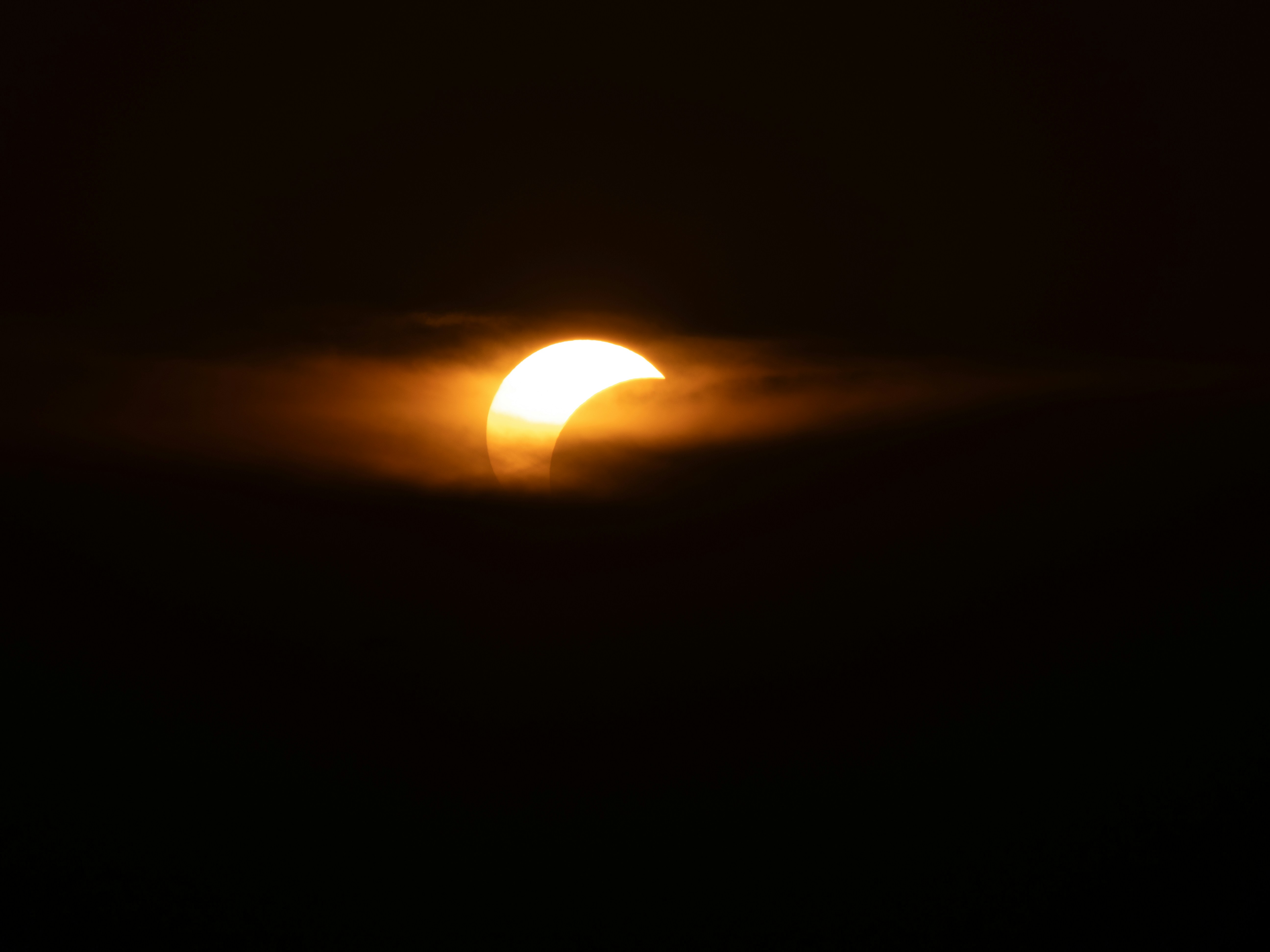 A partial solar eclipse obscured by dark clouds in a black sky