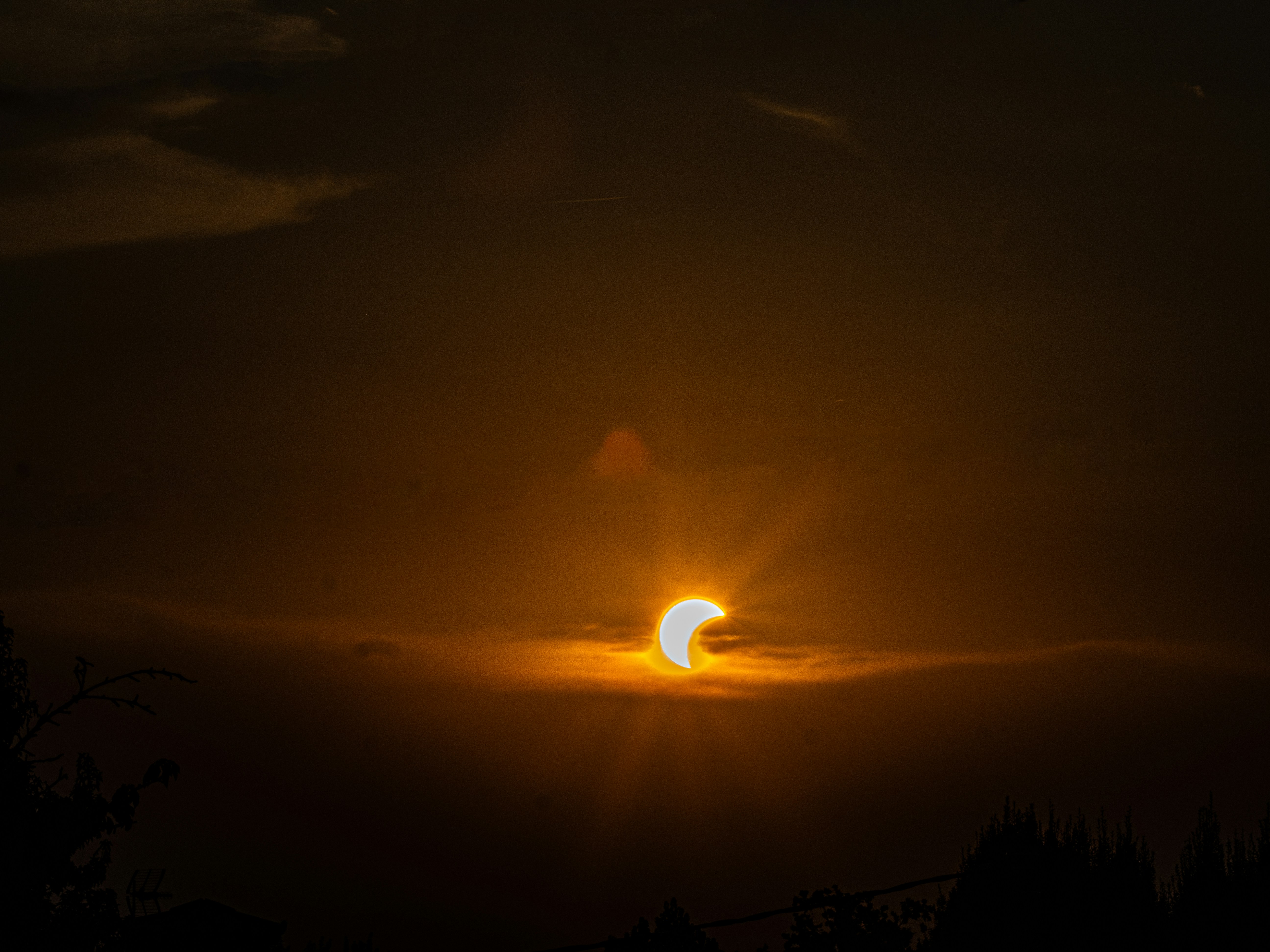 A partial solar eclipse with a crescent sun behind dark clouds