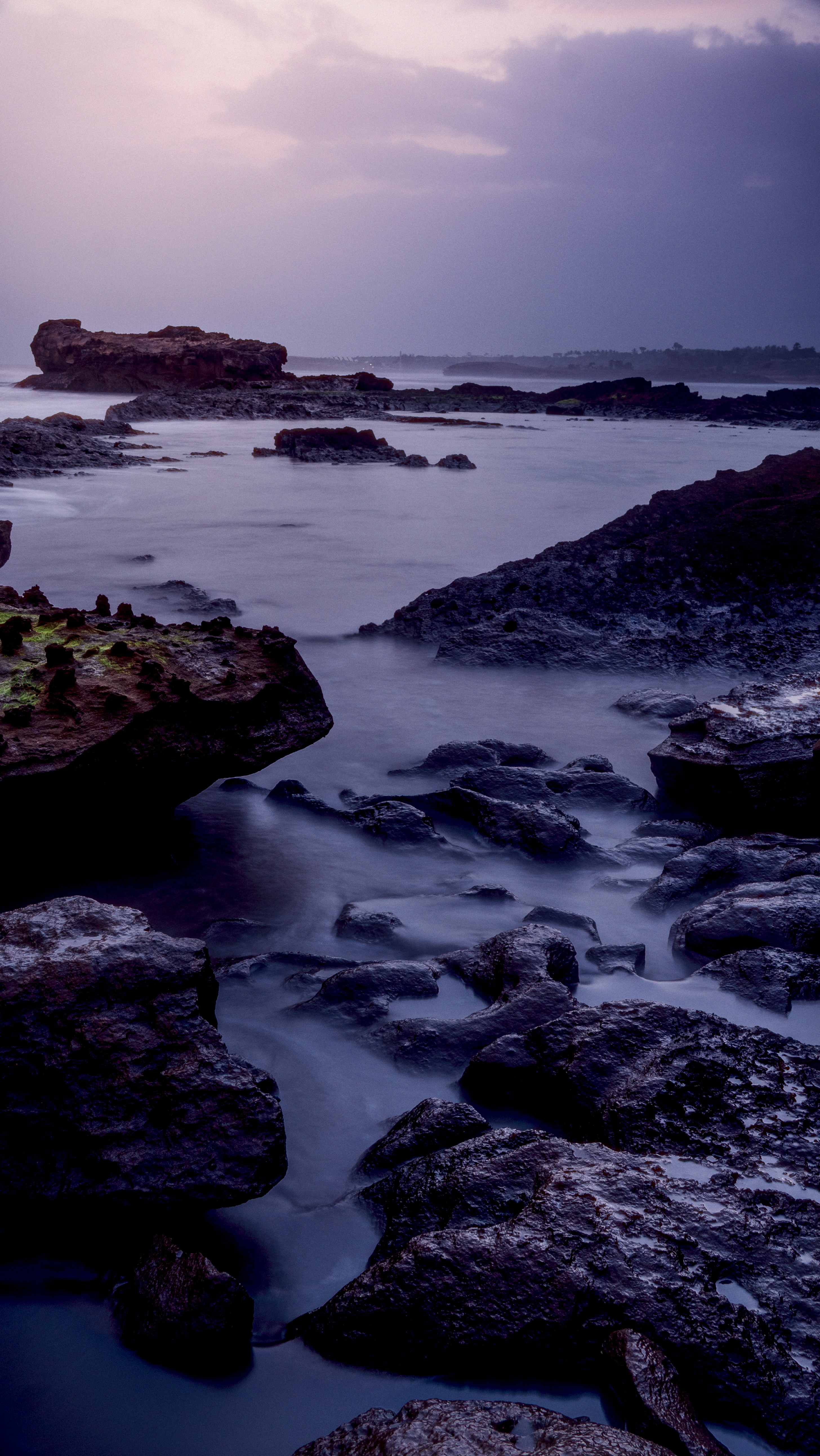 Long exposure of dark rocks in calm water under a purple sky