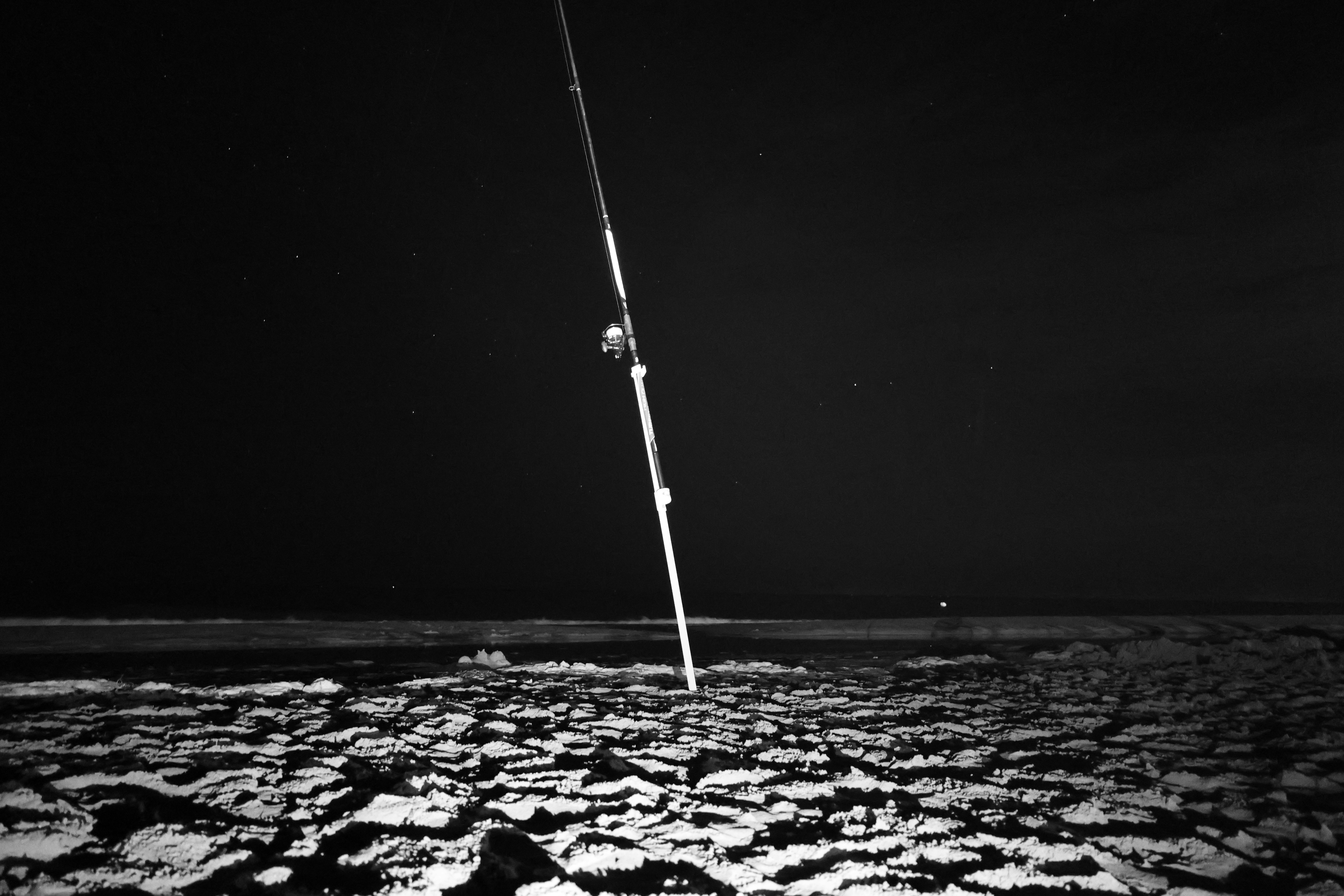 夜の暗い浜辺で砂に刺さった釣り竿