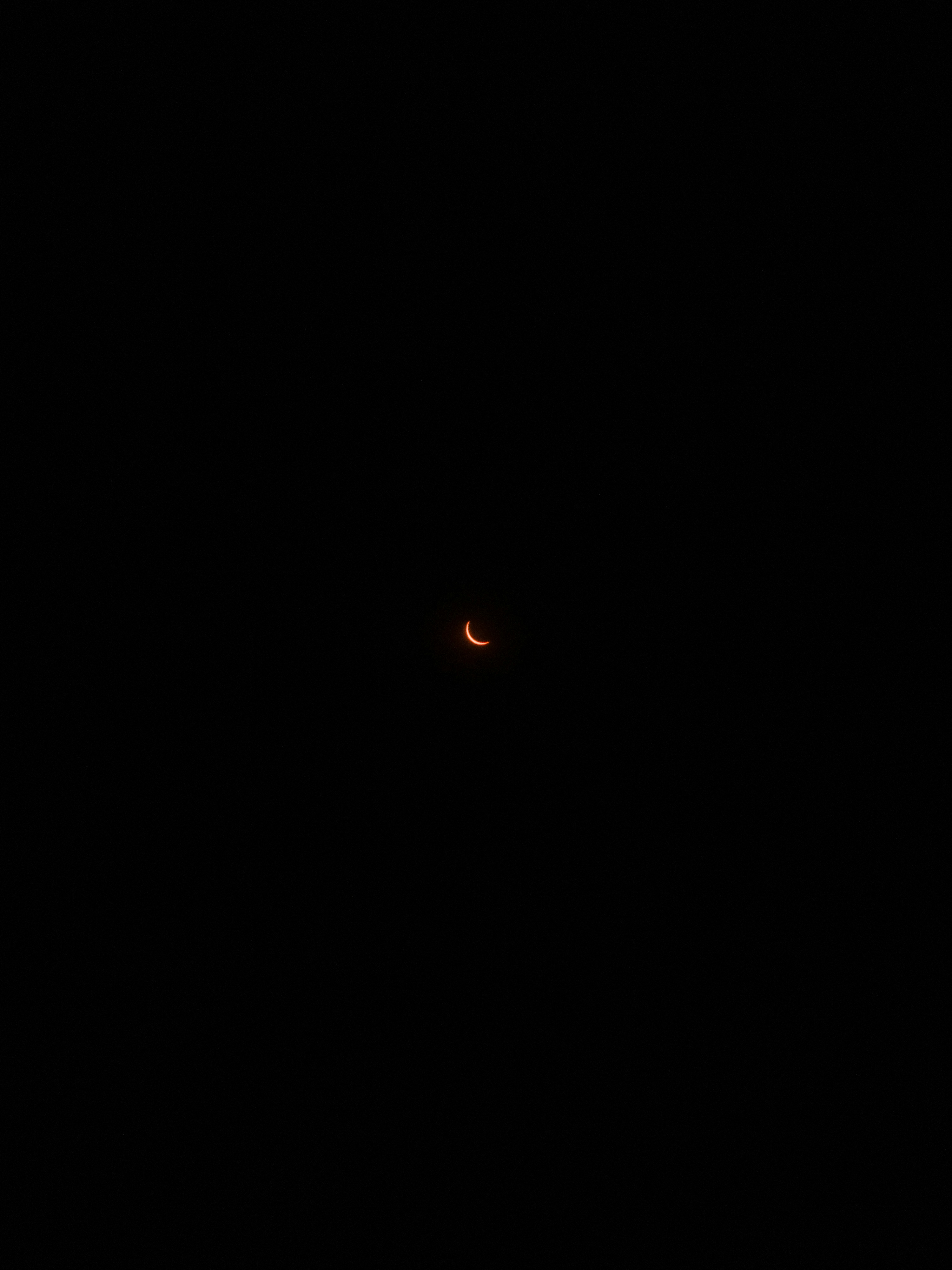 A thin crescent of light from a solar eclipse against a black sky