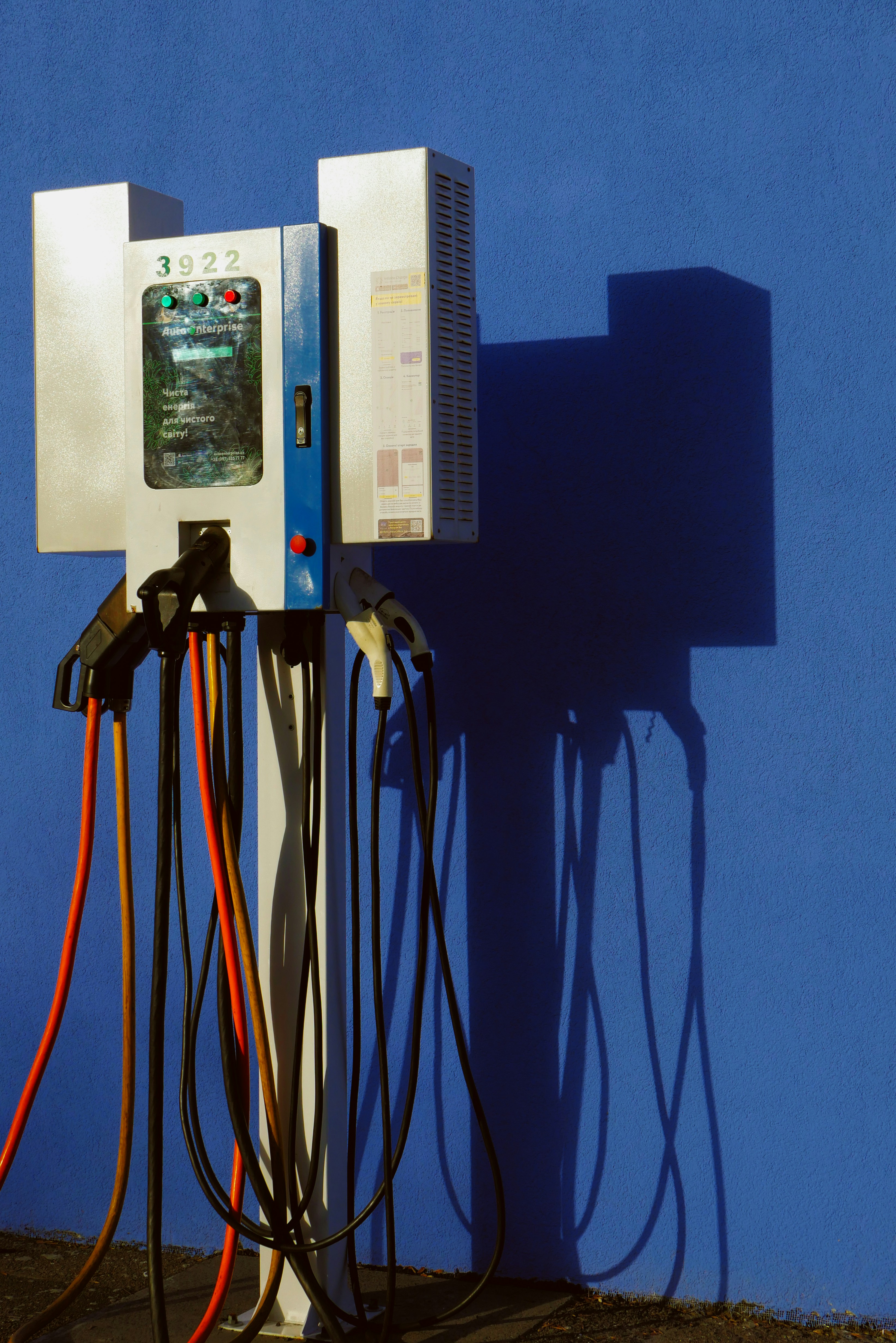Una stazione di ricarica per veicoli elettrici con più cavi contro una parete blu brillante