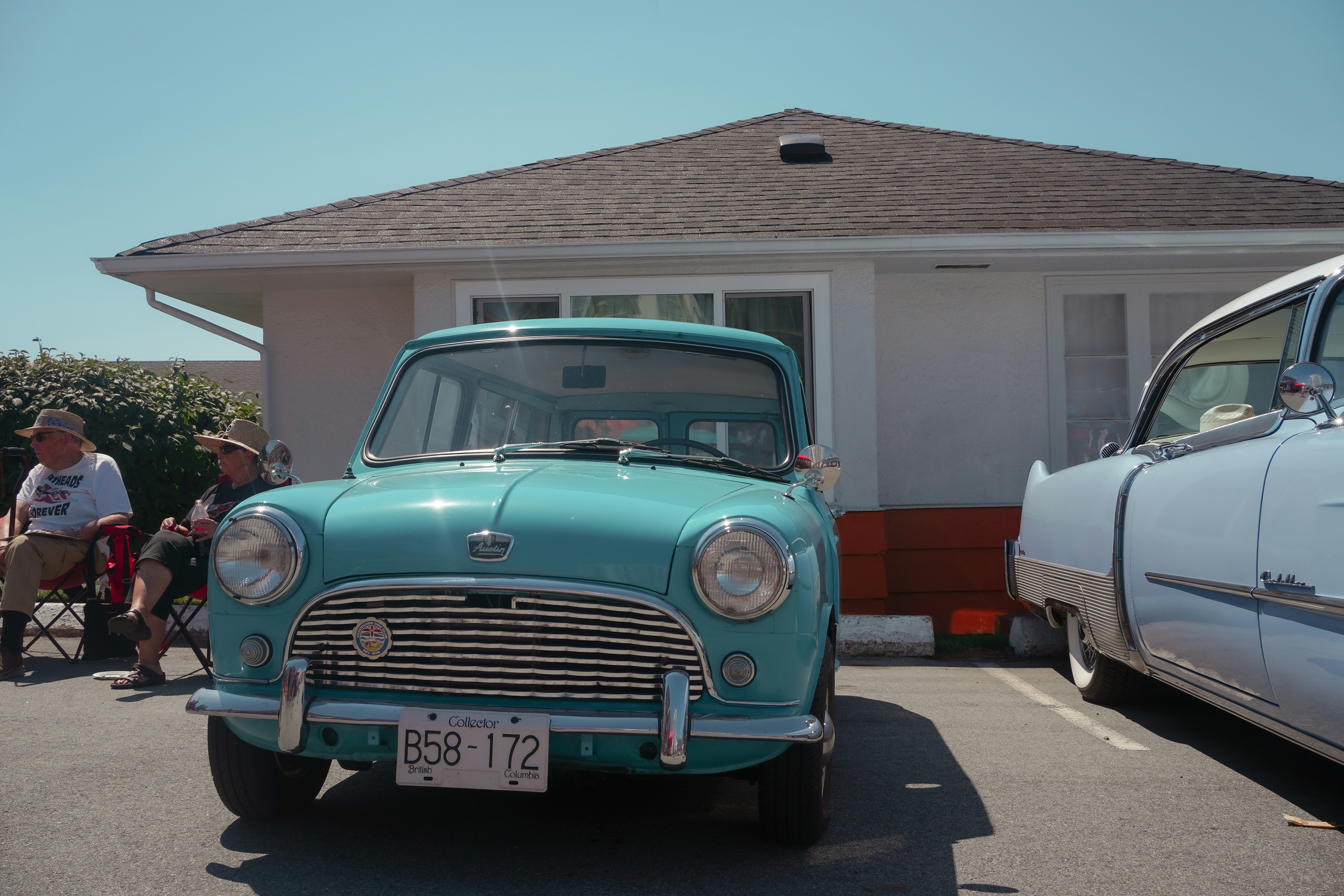 A turquoise Austin Mini parked in front of a house with two people nearby