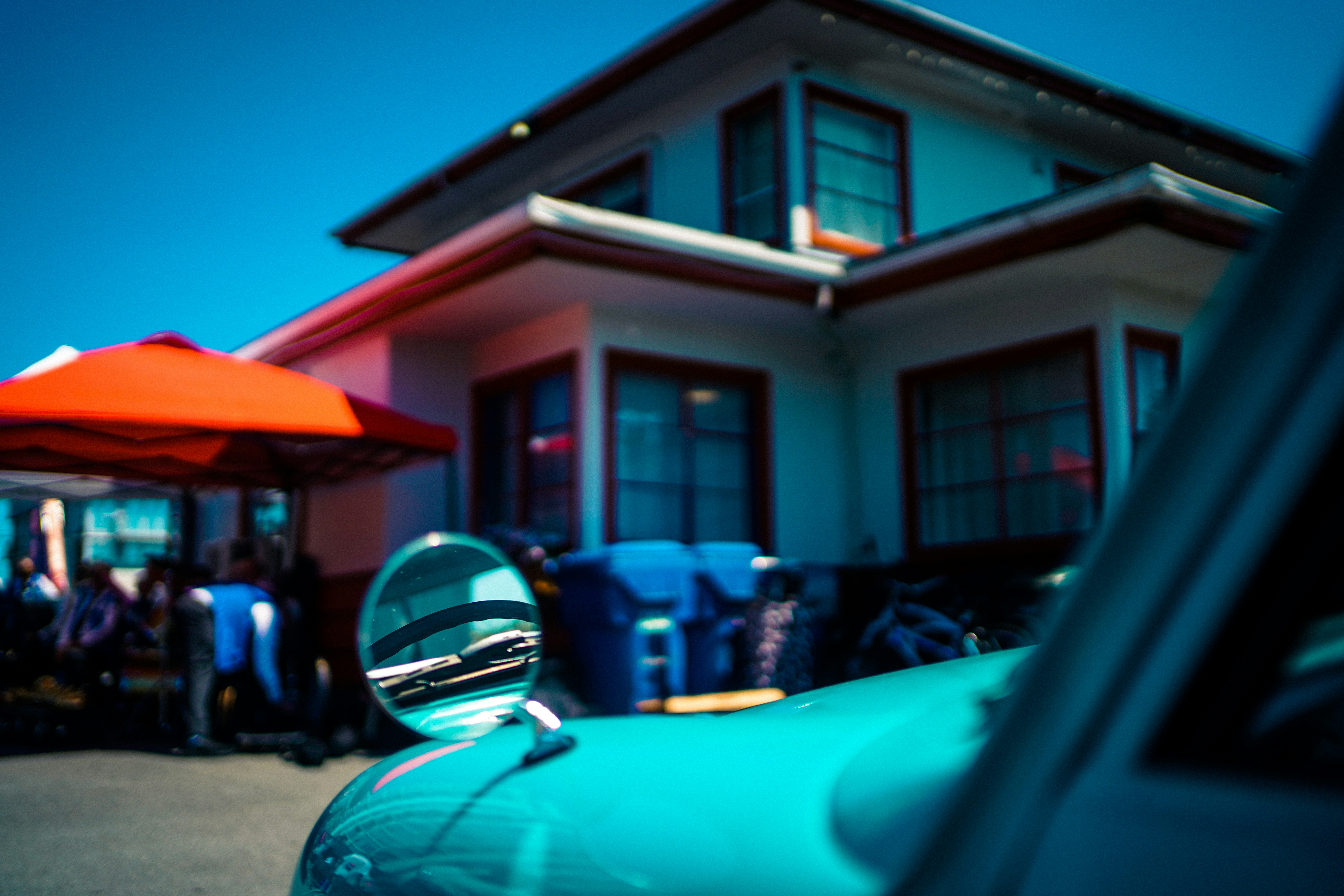 A turquoise car mirror reflecting a windshield in front of a house