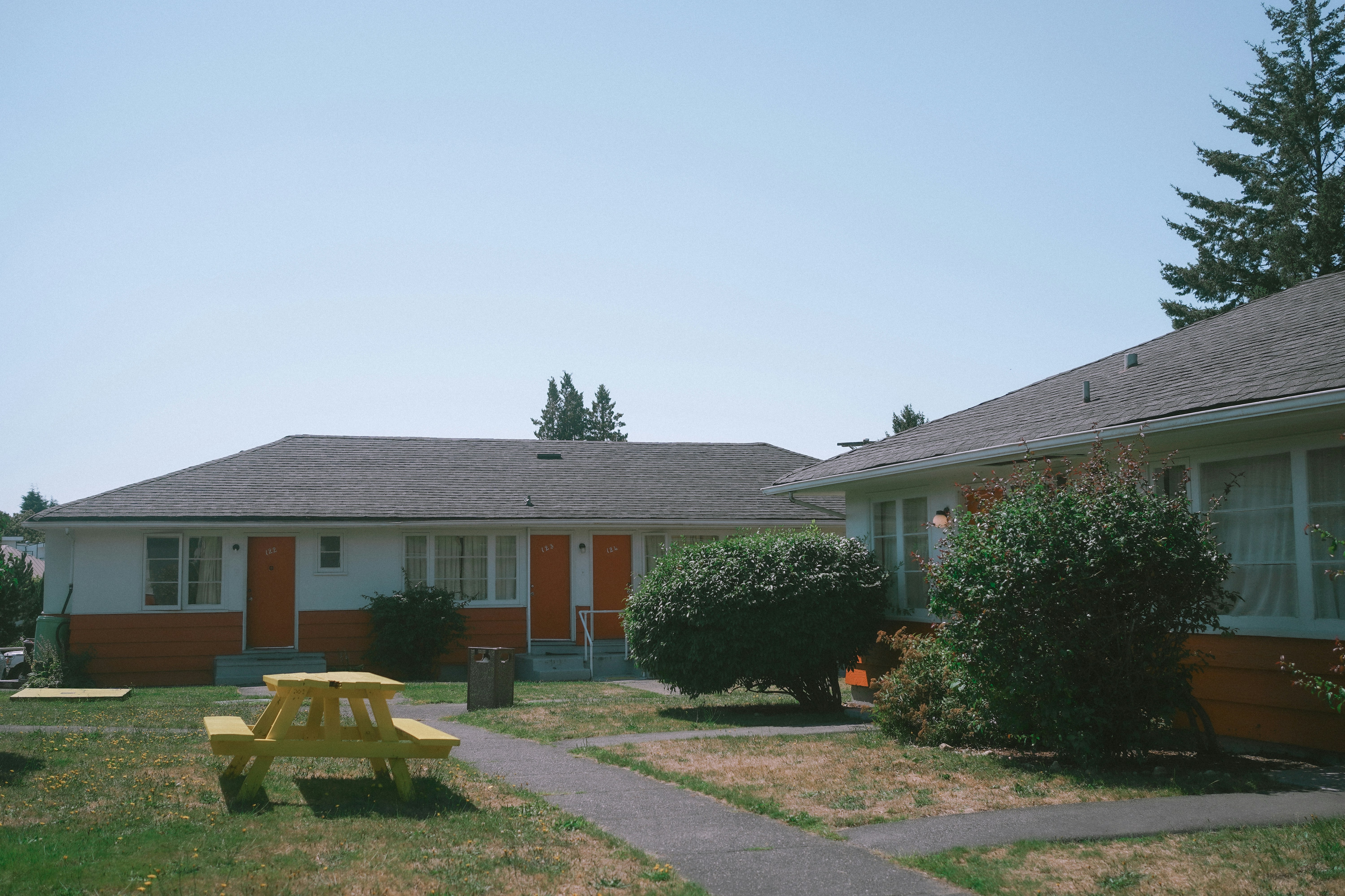 A yellow picnic table on a lawn in front of orange and white motel units