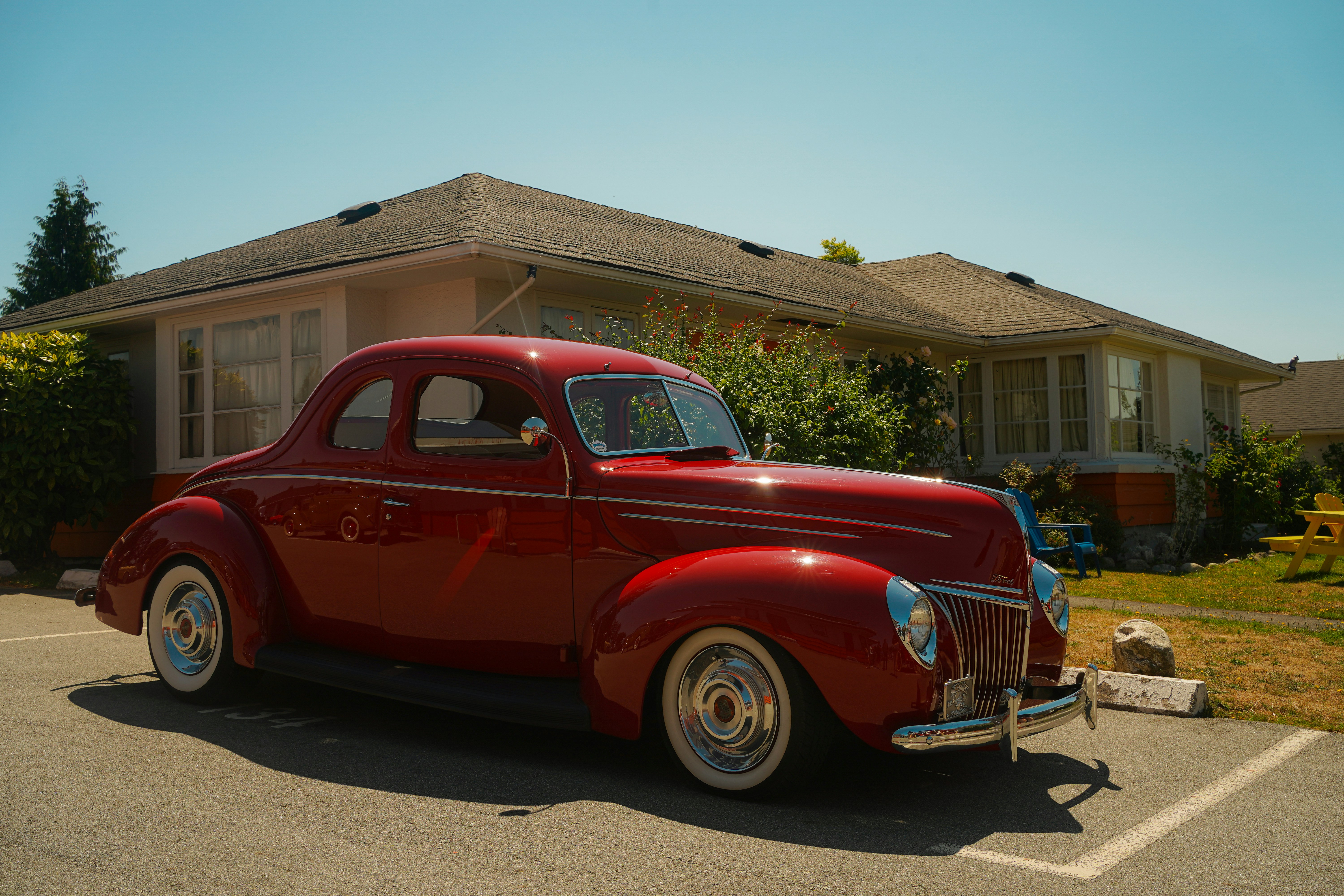 A shiny red vintage car parked in front of a suburban house