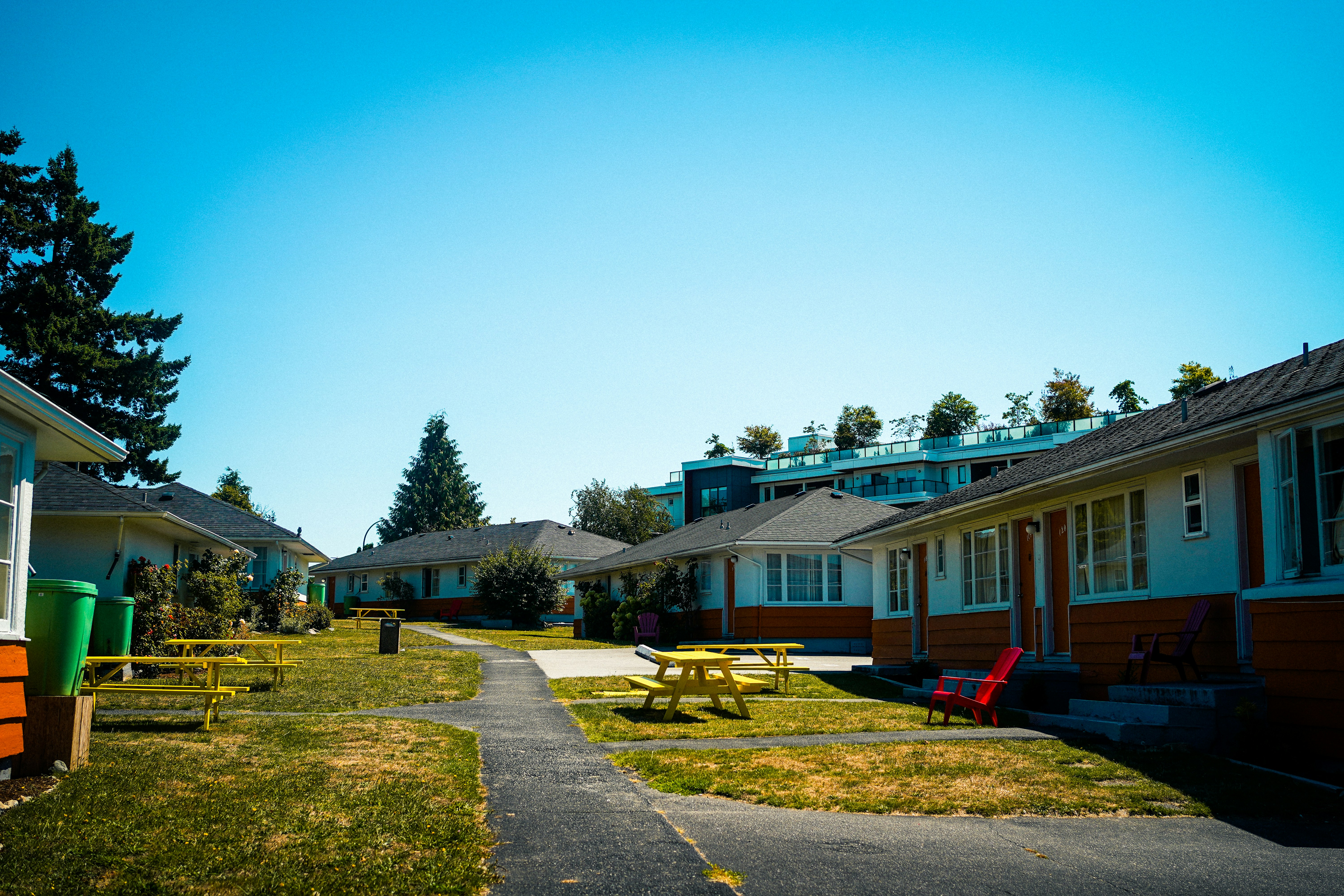 A courtyard with yellow picnic tables and red chairs between low motel buildings