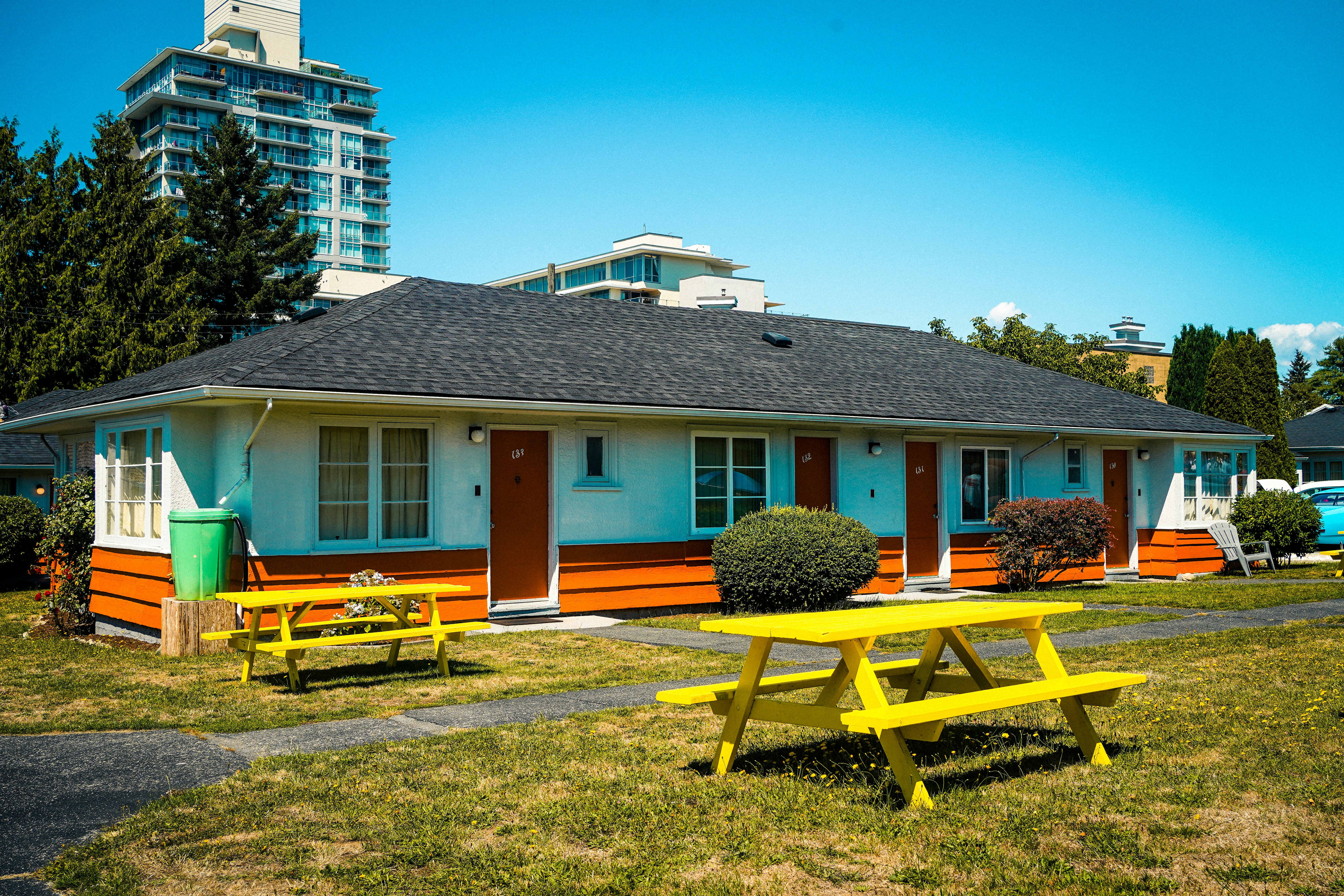 A single-story motel with orange trim and yellow picnic tables on a lawn