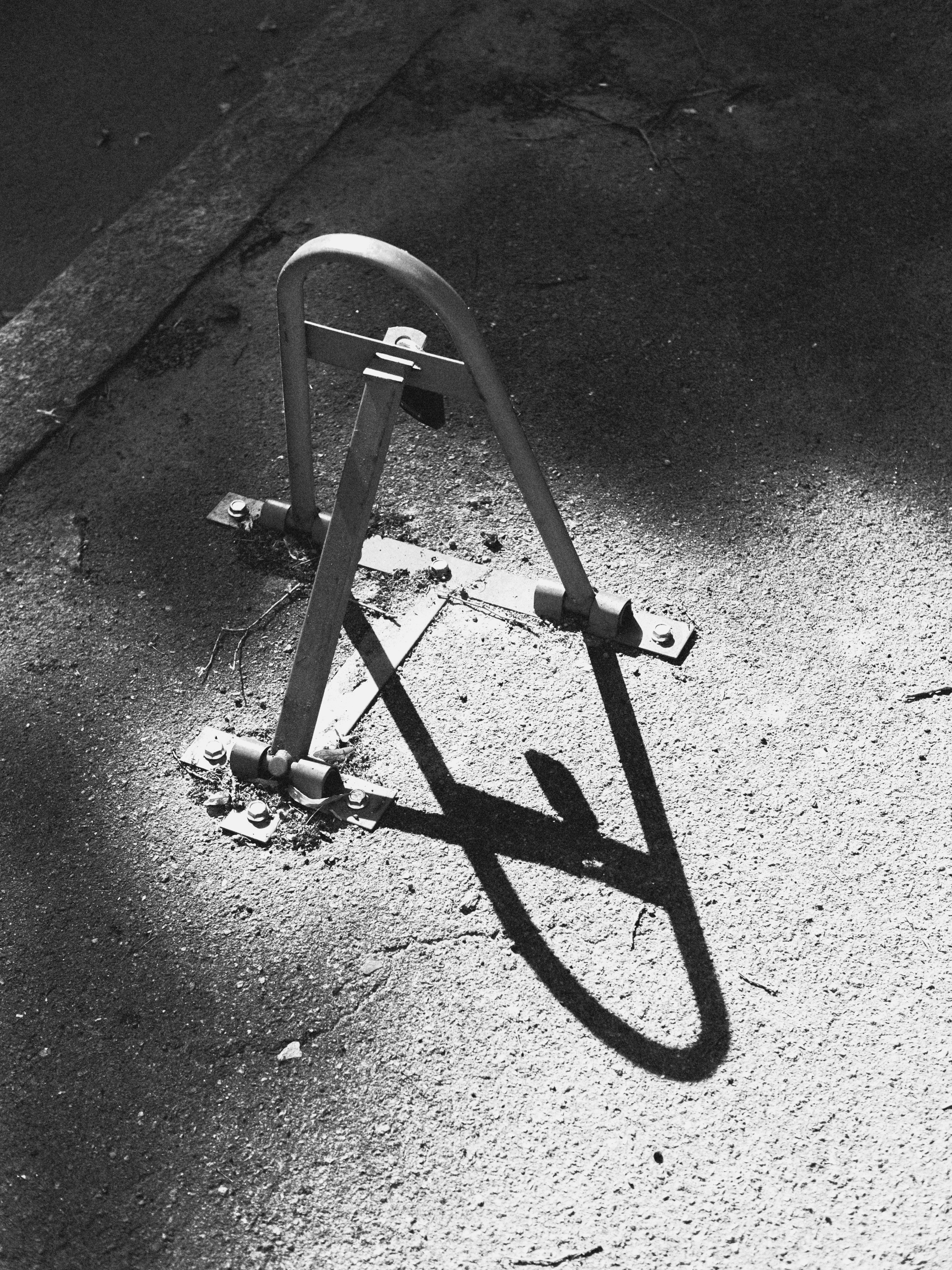 Una barriera di parcheggio metallica fissata all'asfalto con una lunga ombra
