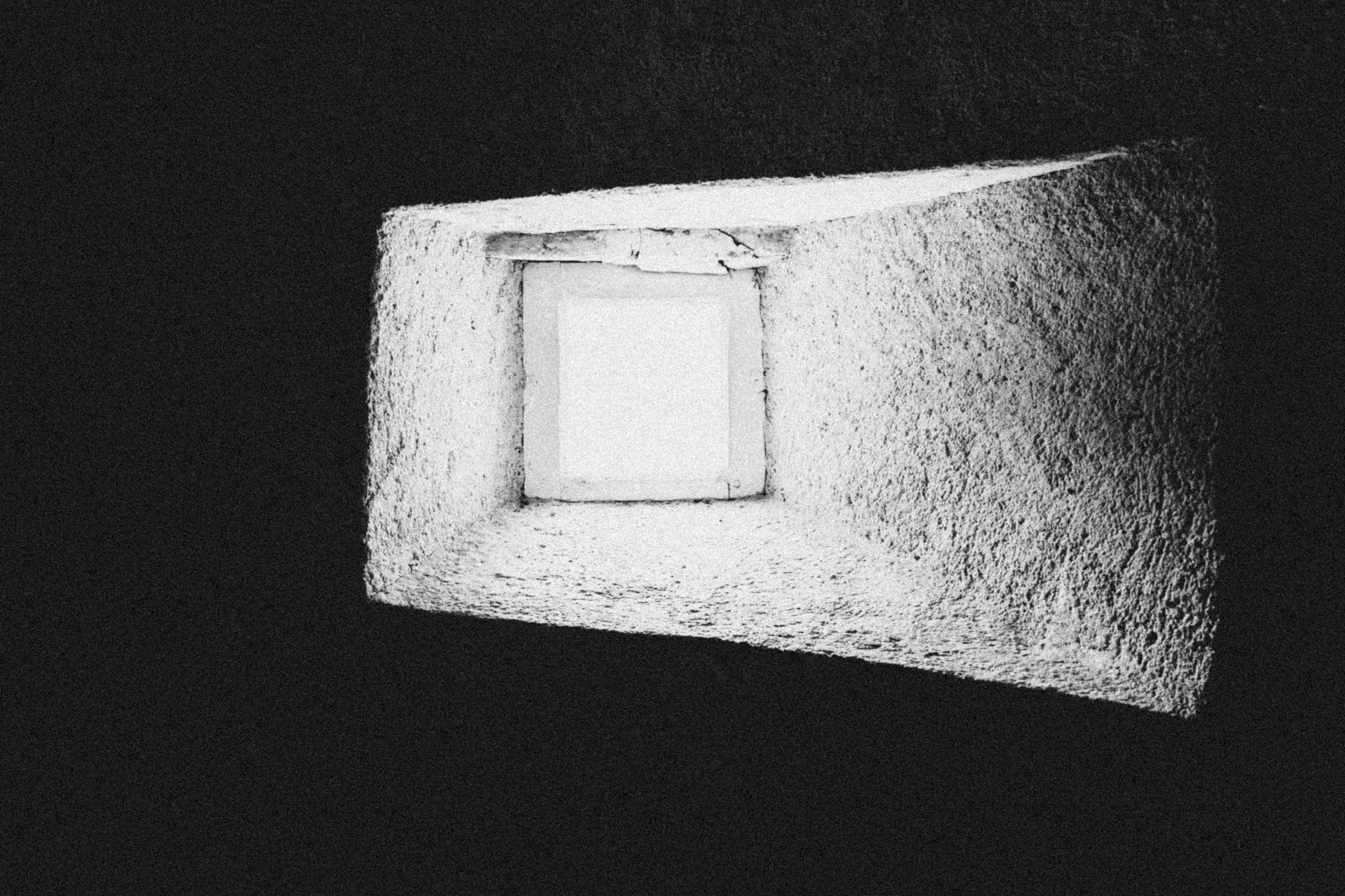 Uma pequena janela quadrada embutida em uma parede branca de textura áspera na escuridão