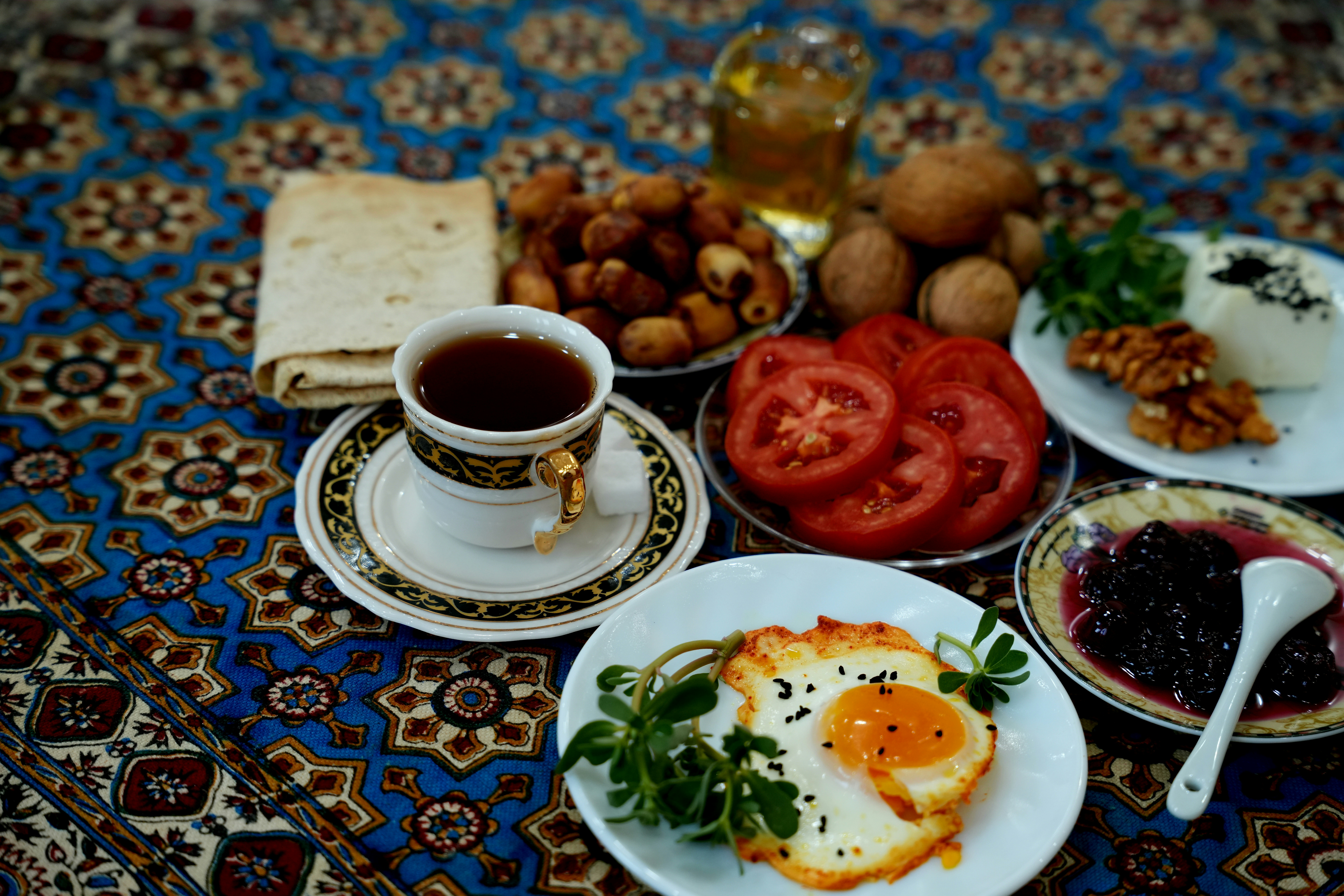 A fried egg, tea, tomatoes, dates, and bread on a patterned tablecloth