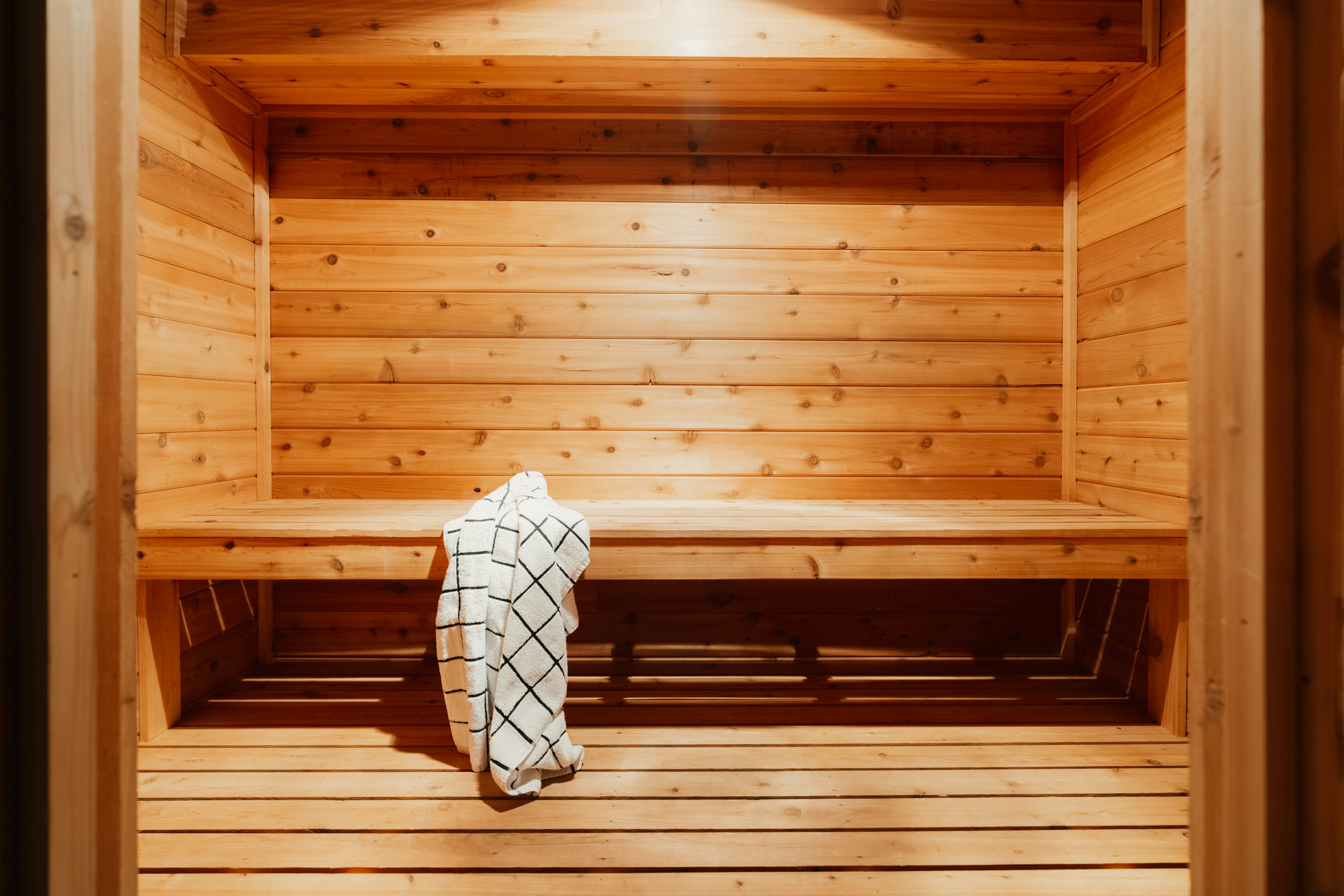 Une serviette blanche à motif noir en grille posée sur un banc de sauna en bois