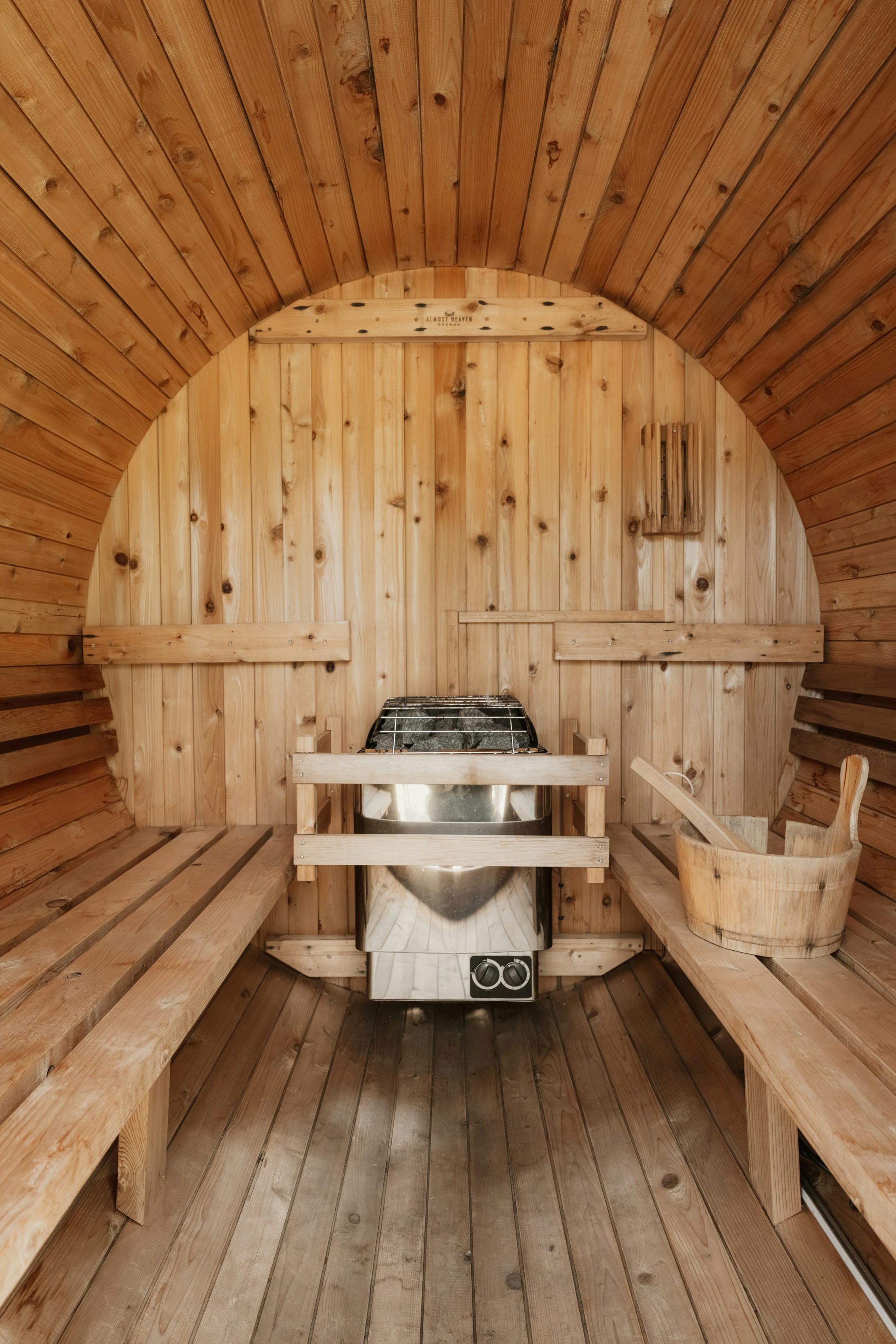 Un intérieur de sauna en tonneau en bois avec un chauffage en métal et un seau en bois