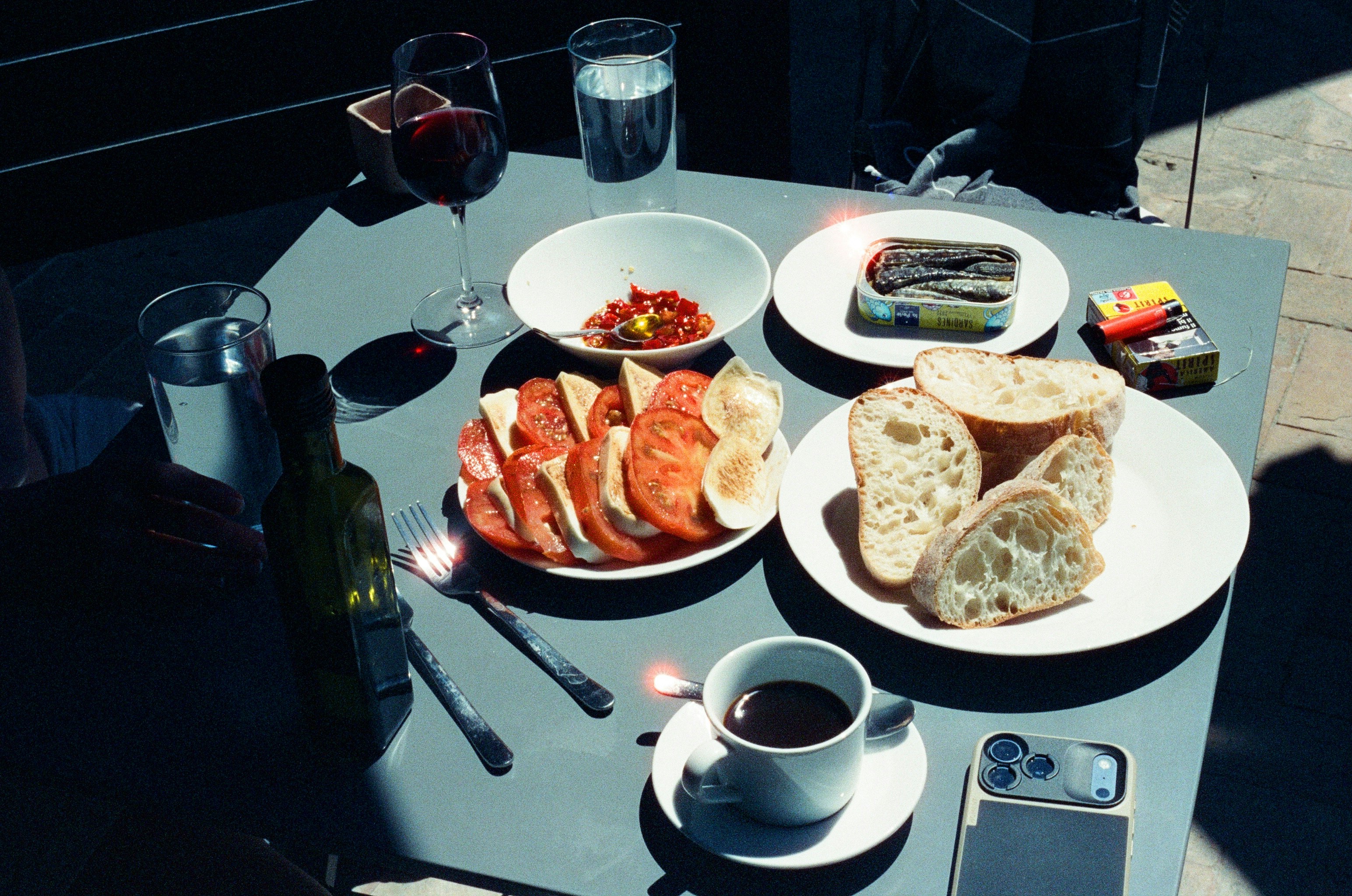A table with bread, tomato and mozzarella salad, sardines, wine, and coffee