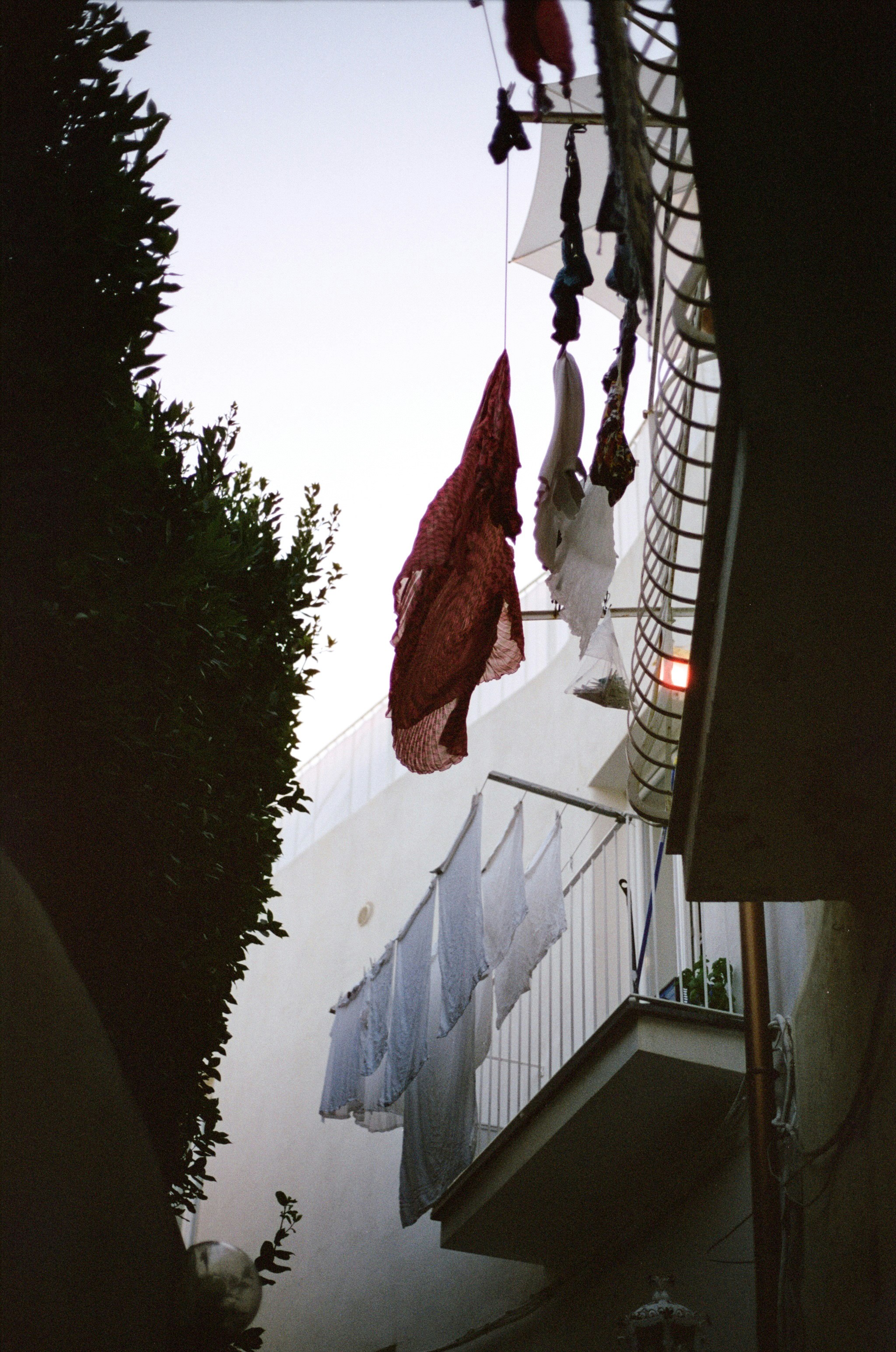 Laundry hanging on lines between balconies of white buildings with green foliage