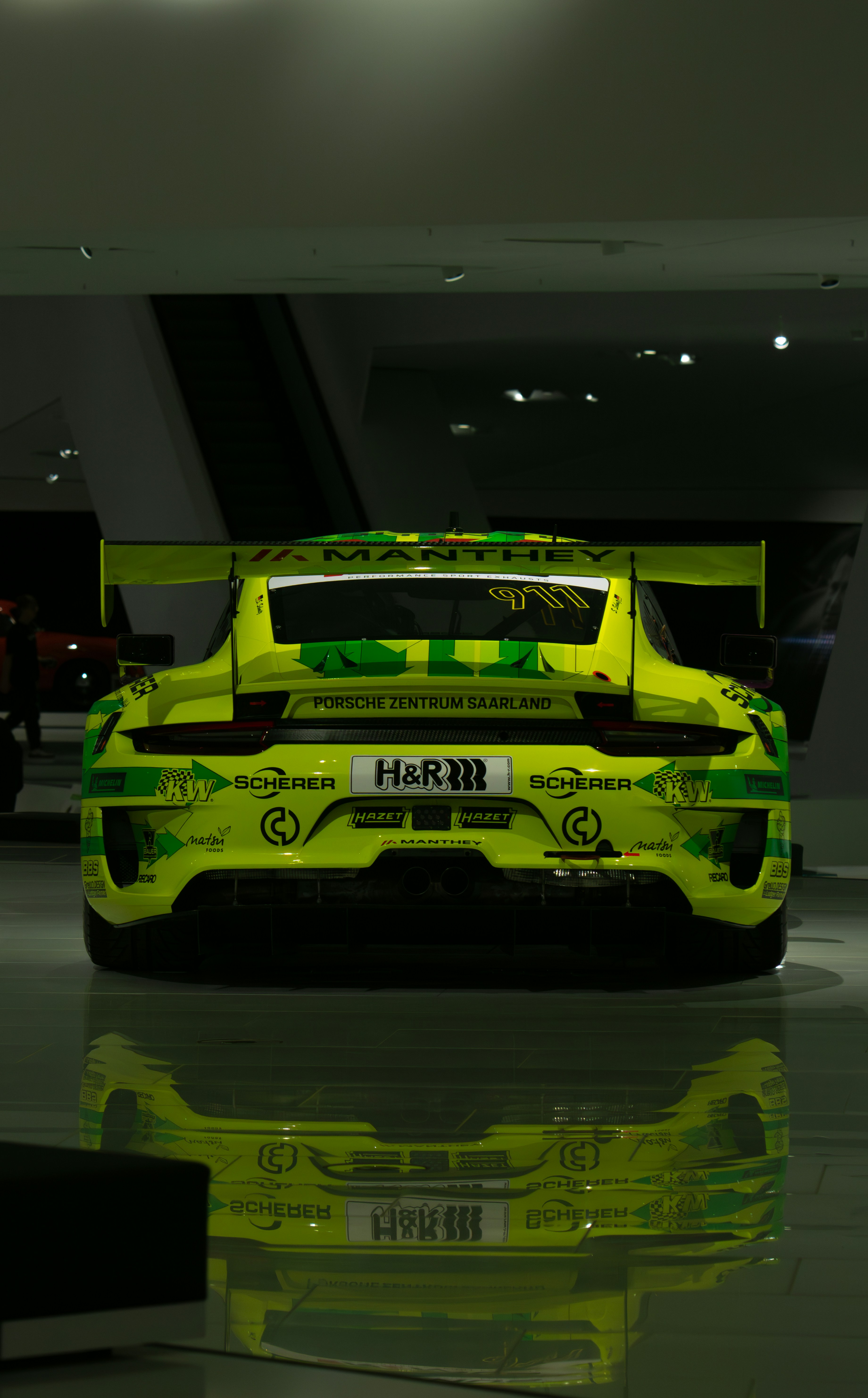 A bright neon yellow Porsche 911 race car with sponsor decals in a showroom