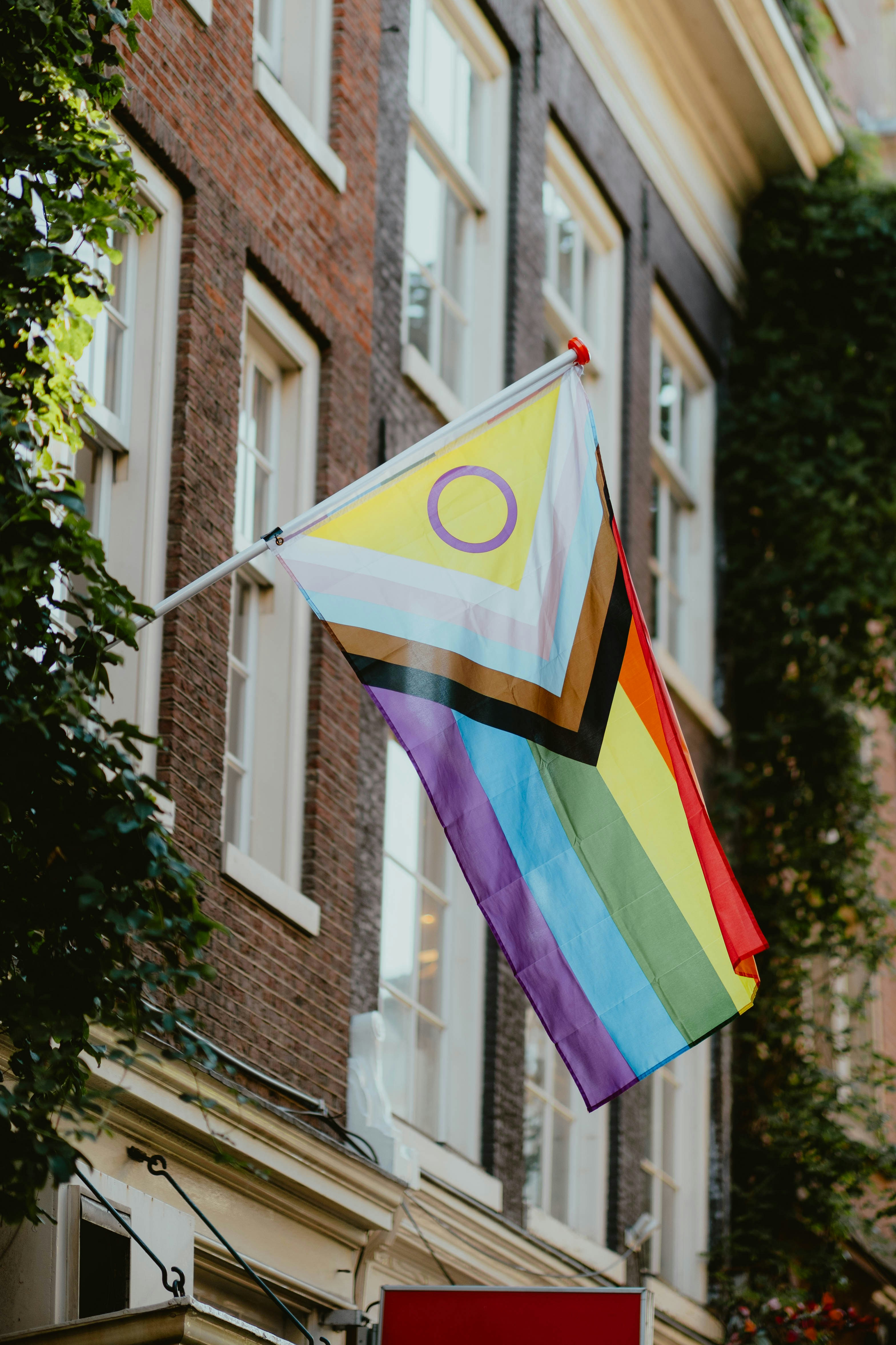 An intersex-inclusive progress pride flag hanging from a brick building facade