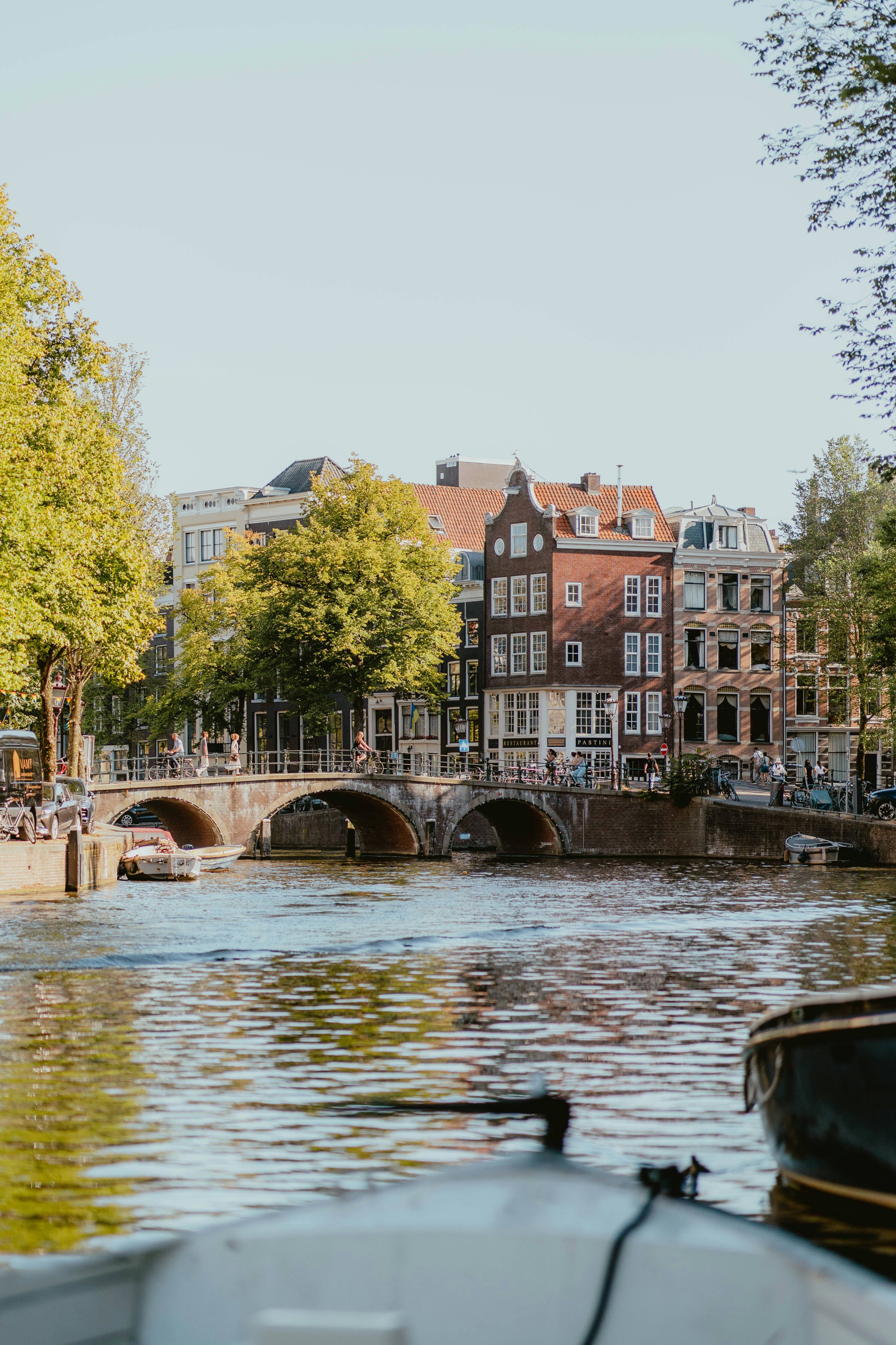 A stone bridge over a canal in Amsterdam with historic buildings and trees