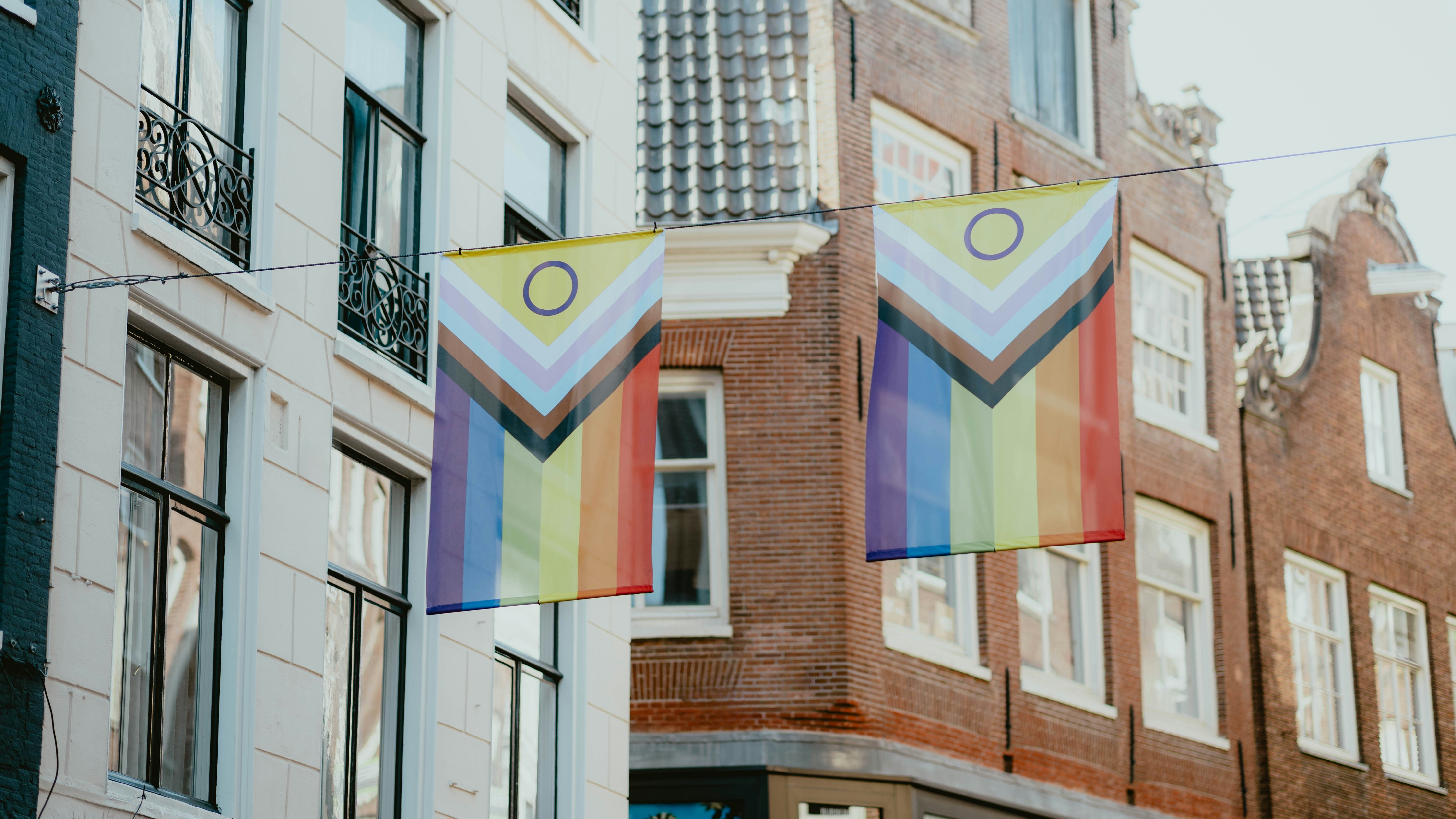 Deux drapeaux de la fierté du progrès inclusifs intersexes suspendus entre des bâtiments historiques en brique à Amsterdam