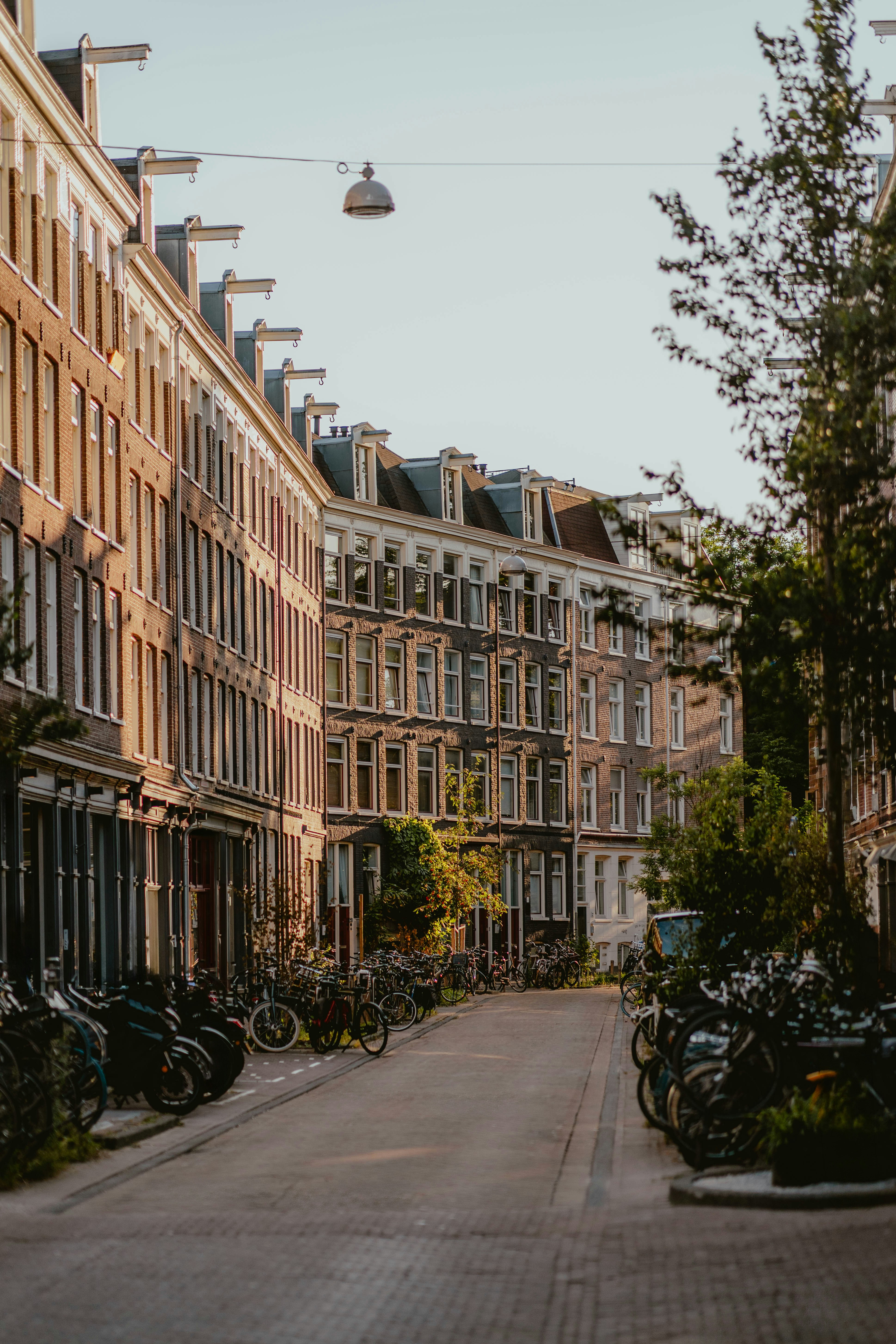 Une rue étroite d’Amsterdam bordée de hauts immeubles en brique et de nombreux vélos garés