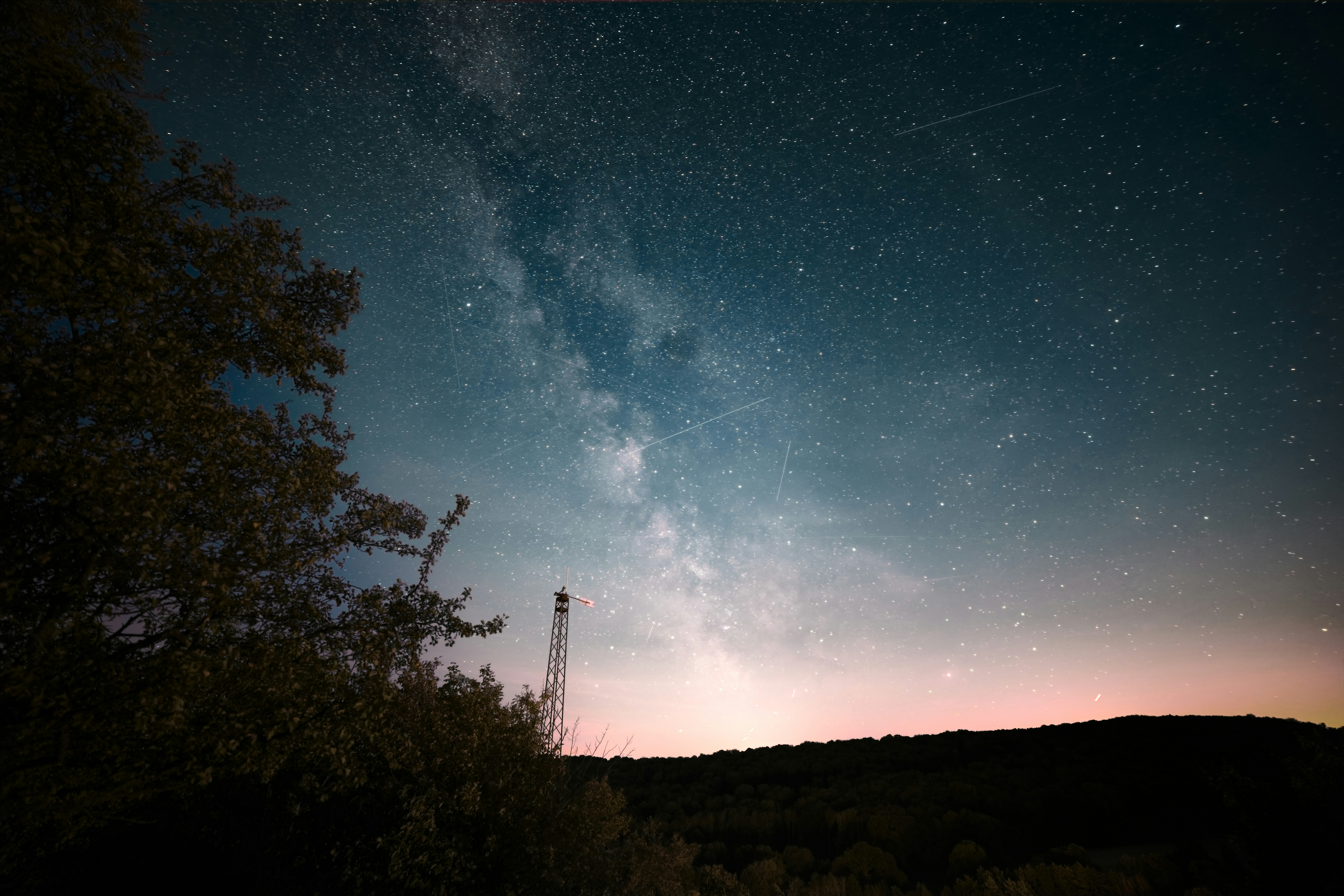 The Milky Way galaxy above a dark silhouette of trees and a radio tower