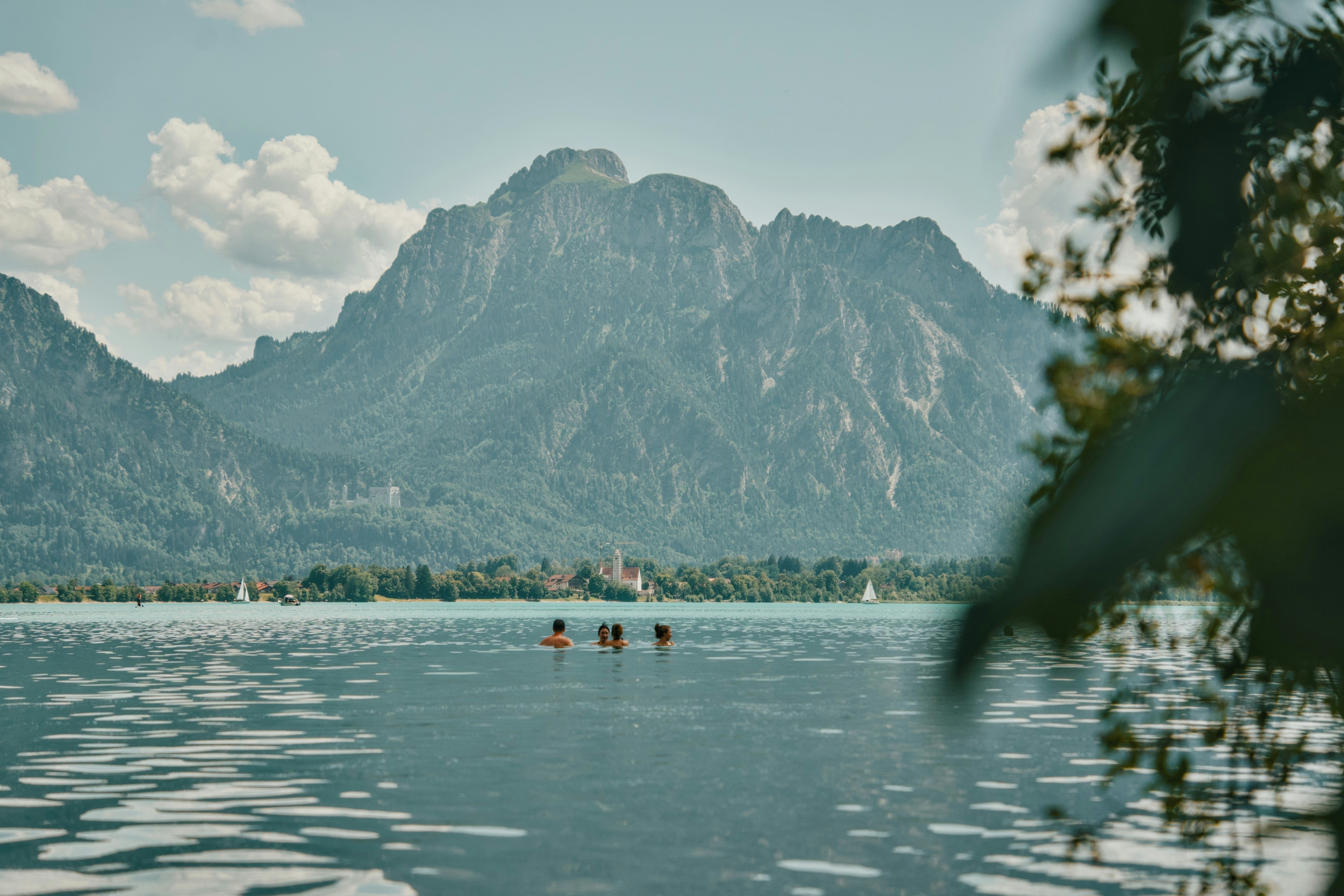Tre persone che nuotano in un grande lago sotto una catena montuosa imponente