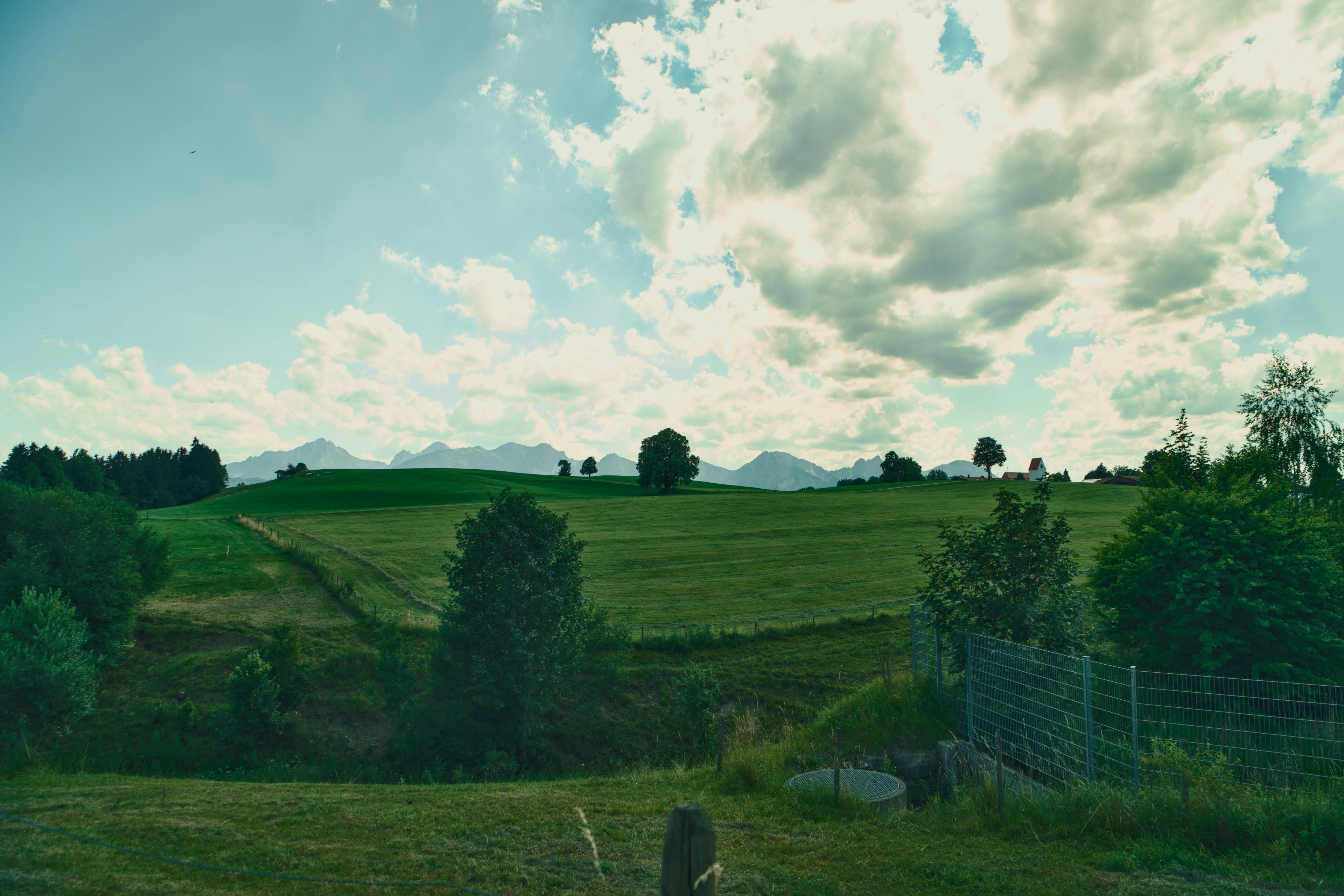 Green rolling hills and distant mountains under a sky with scattered white clouds