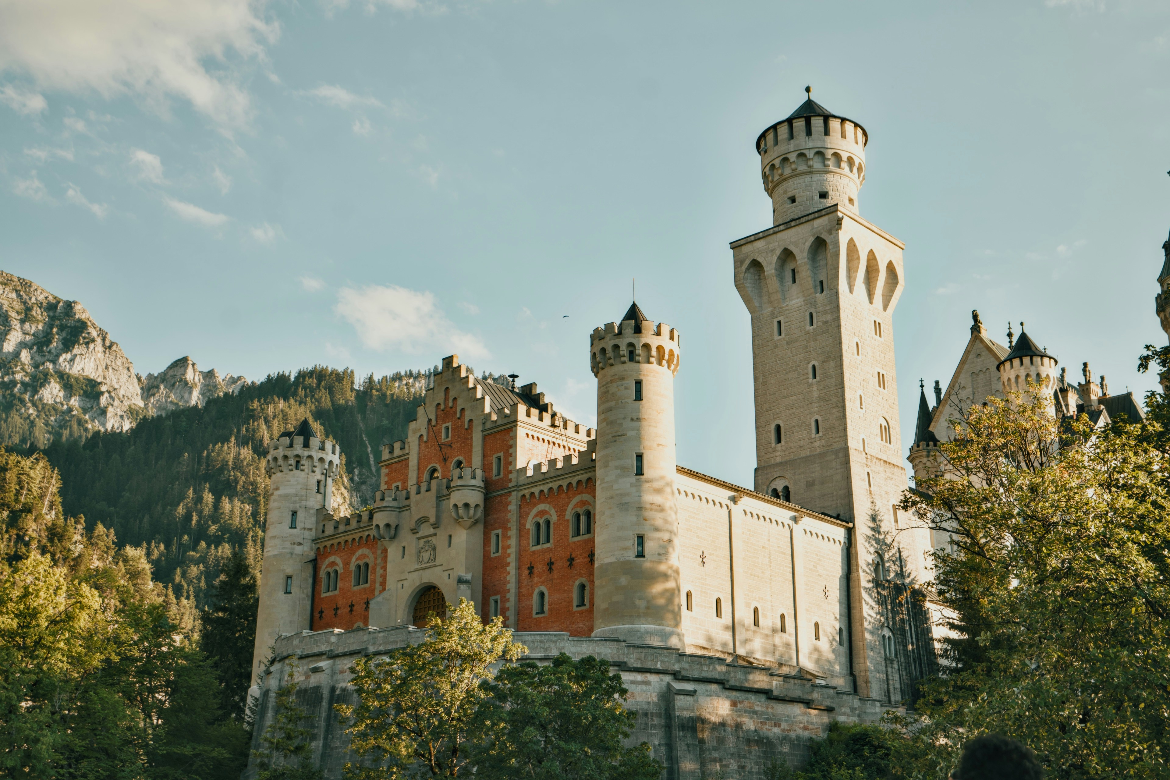 Castello di Neuschwanstein con torri in pietra e mura in mattoni rossi contro una foresta di montagna