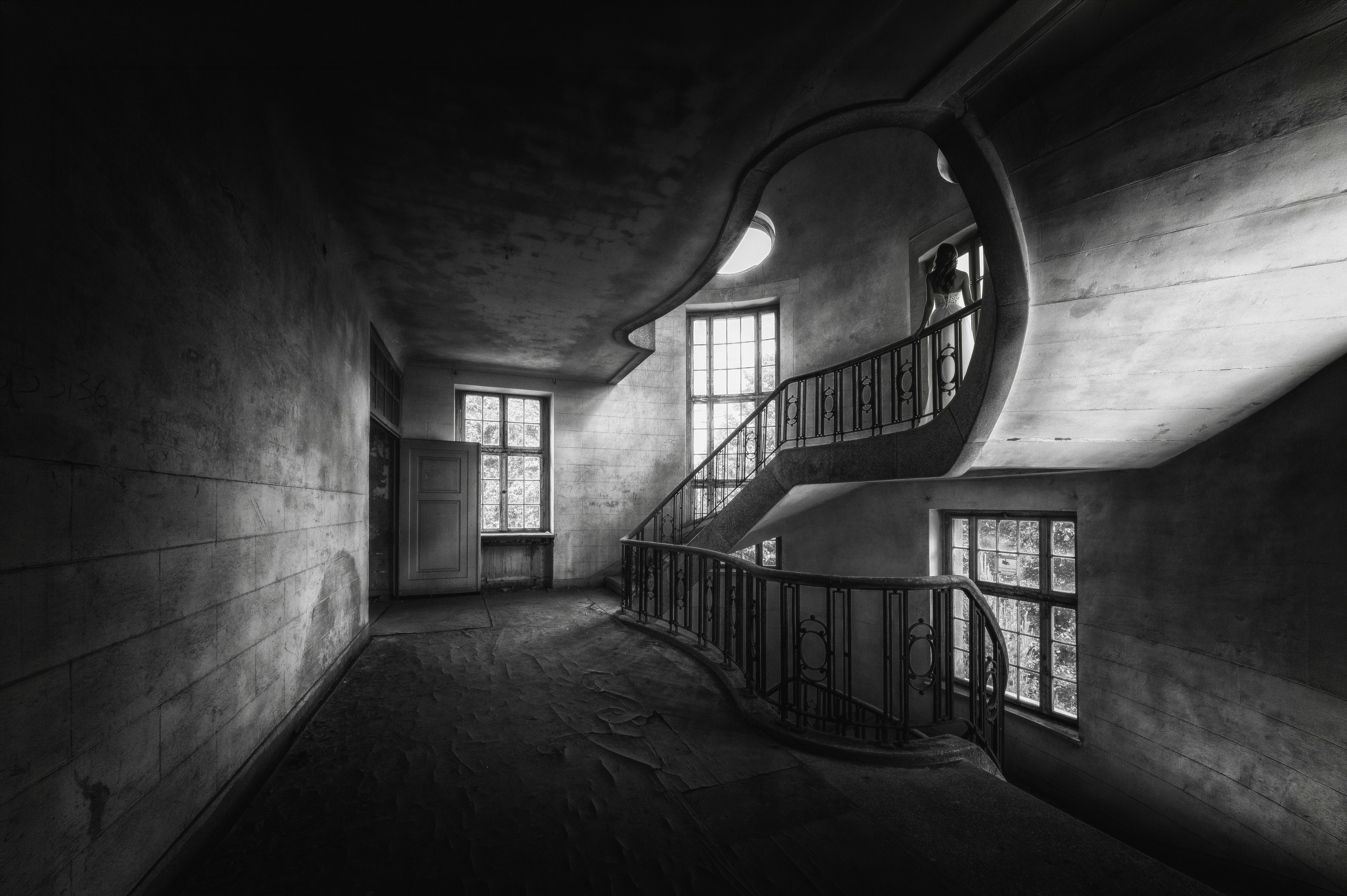 A person in a white dress on a curved staircase in a derelict building
