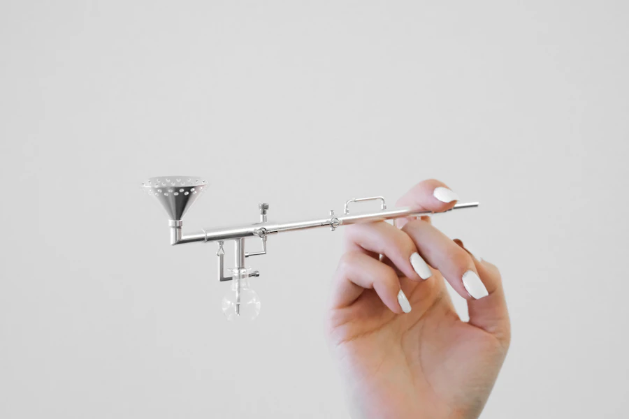 A hand with white manicured nails holding a small silver airbrush tool