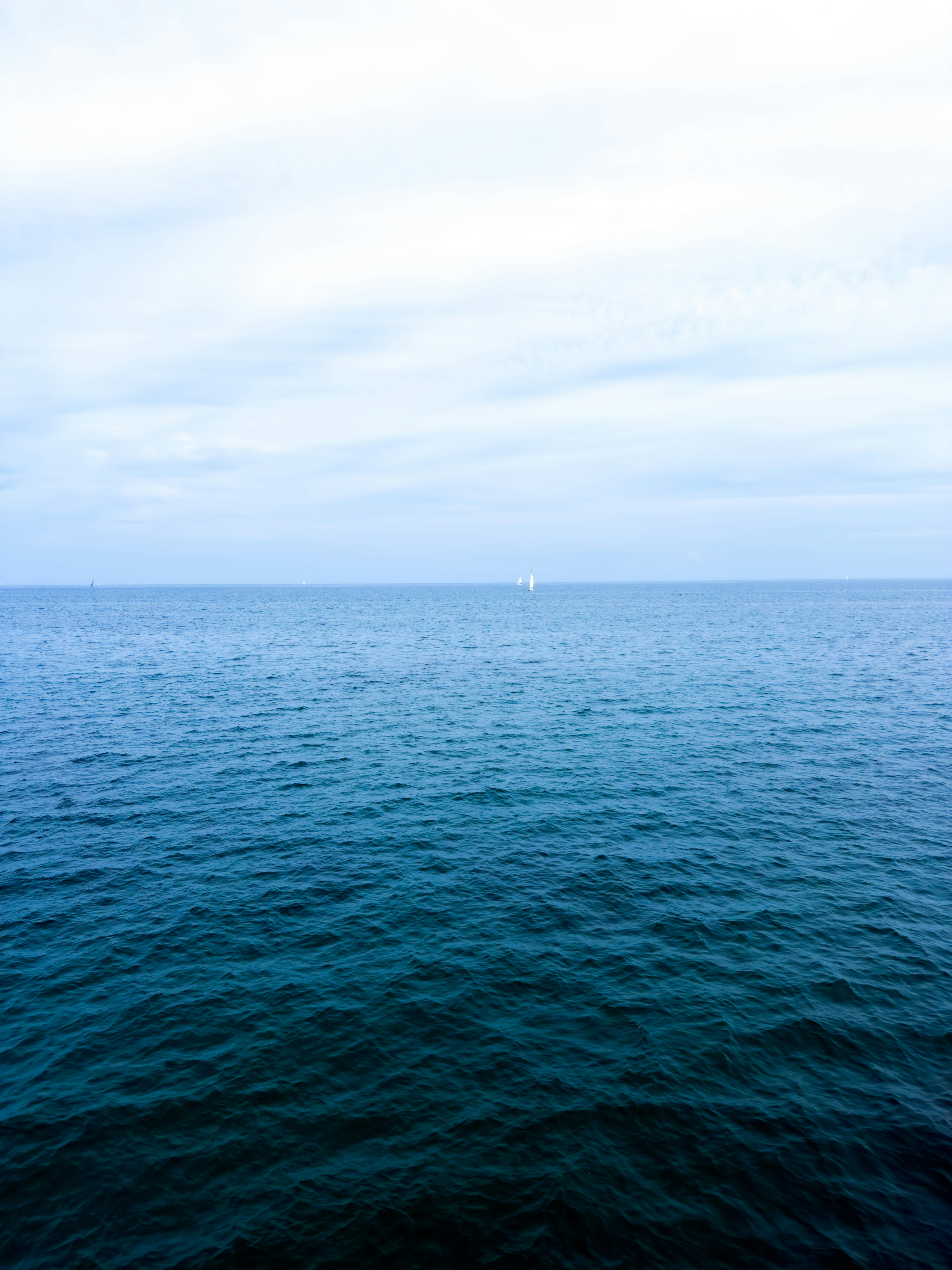 A vast blue ocean under a cloudy sky with distant white sailboats