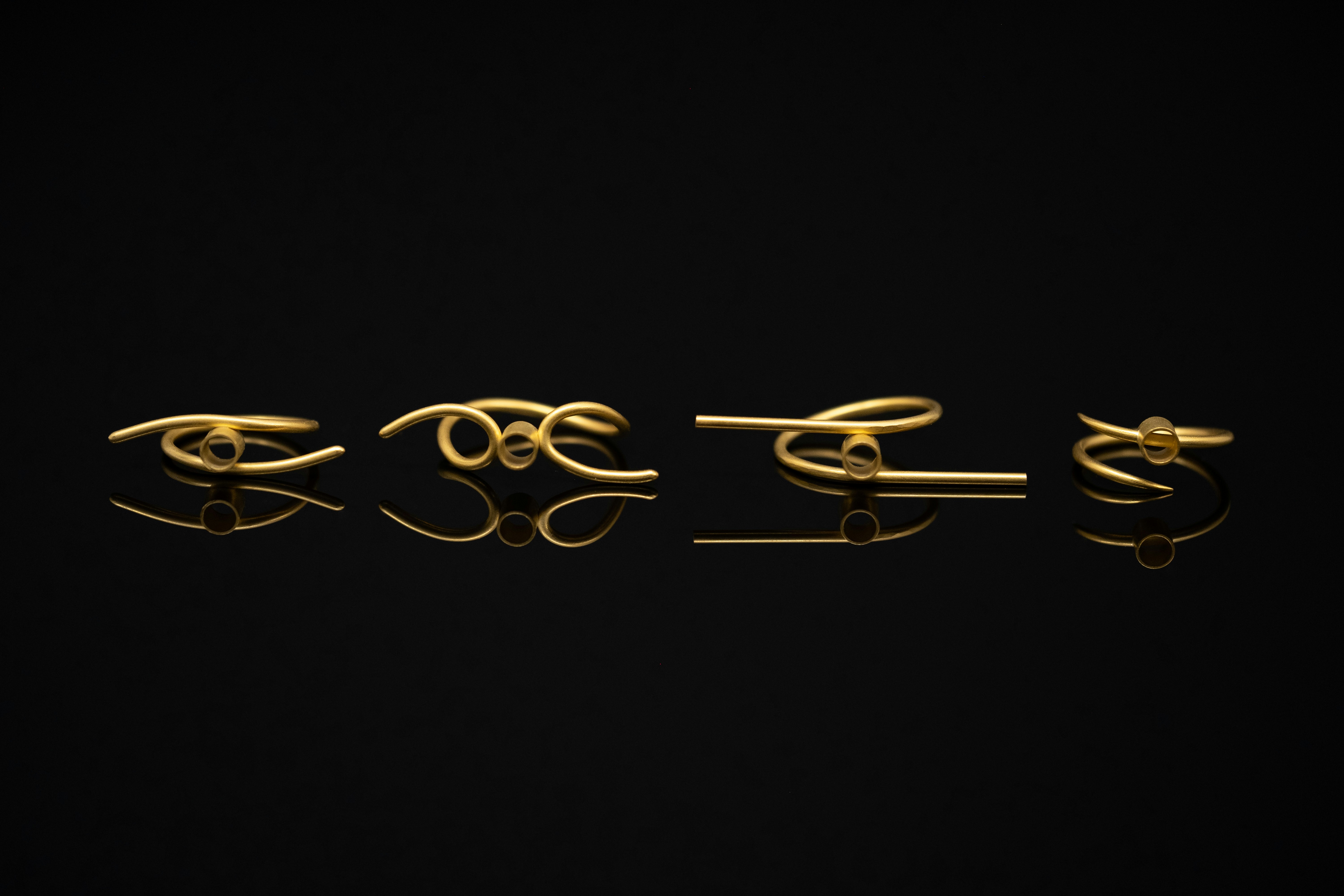 Four unique gold rings arranged in a row on a reflective black surface