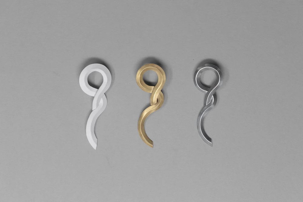 Sculptural silver and gold pendant forms against a gray background.