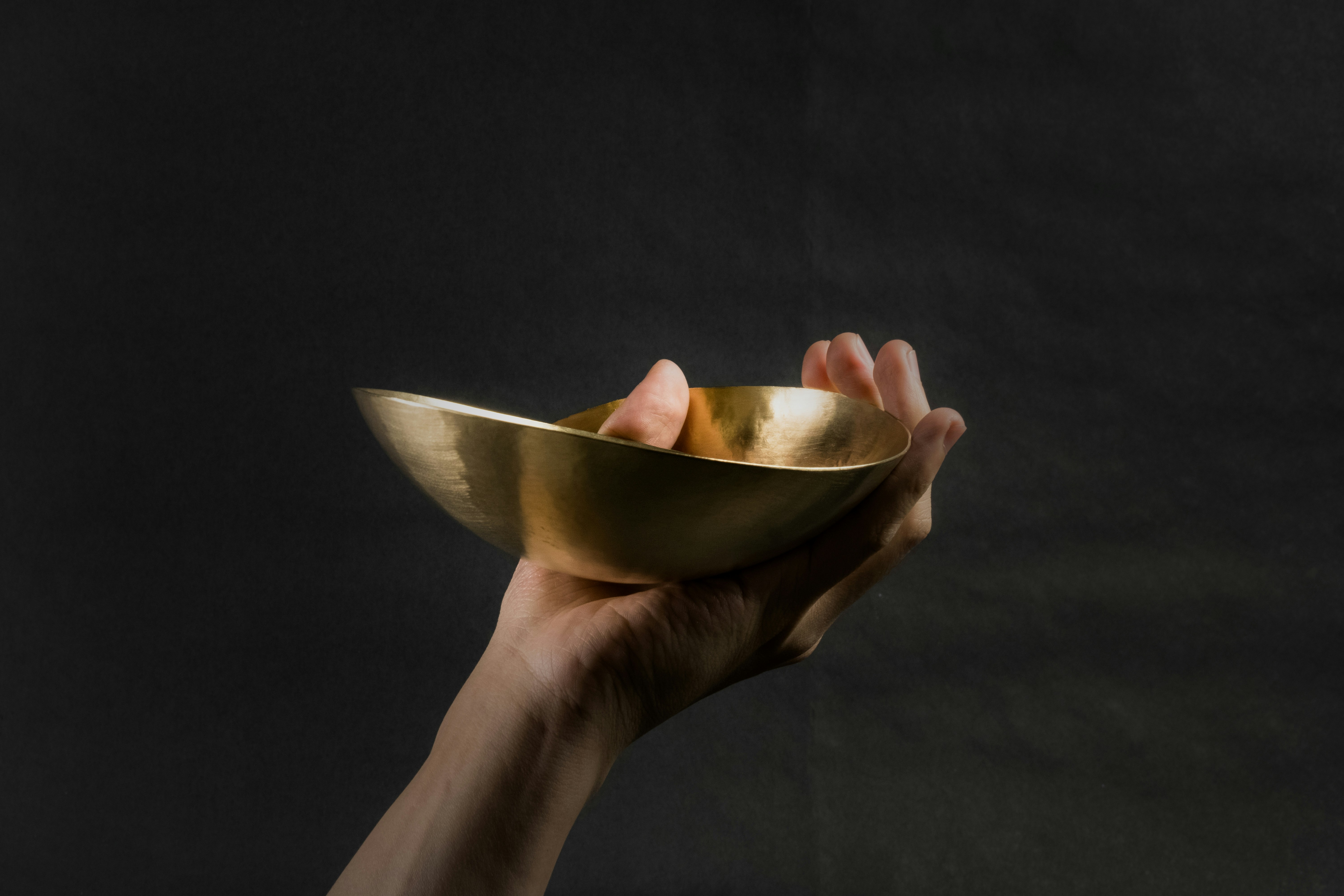 Hand holding a traditional brass bowl of Indian food