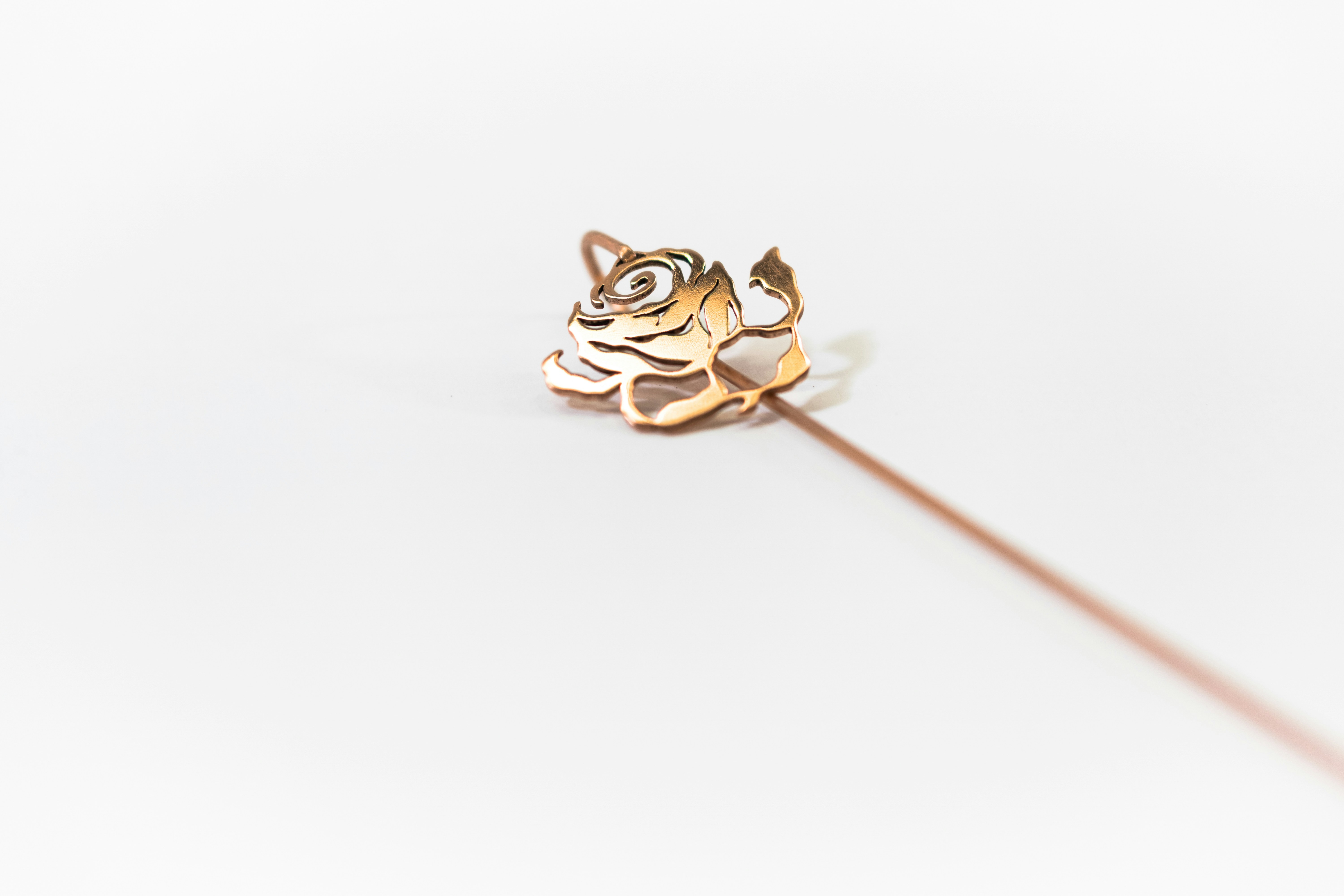 Fotomural A gold rose pin with a cutout design on a white surface