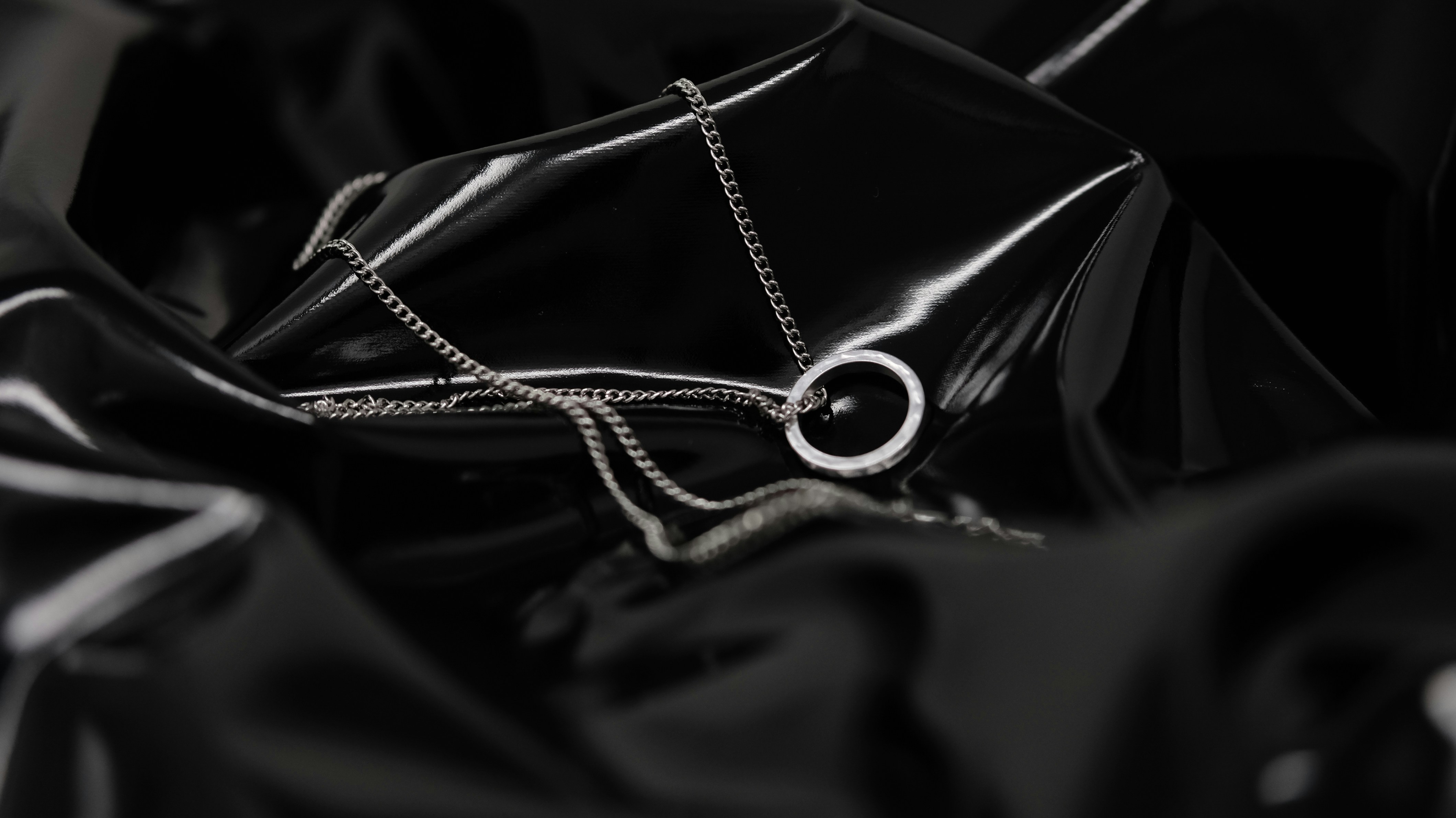 A silver chain necklace with a circular pendant on shiny black fabric