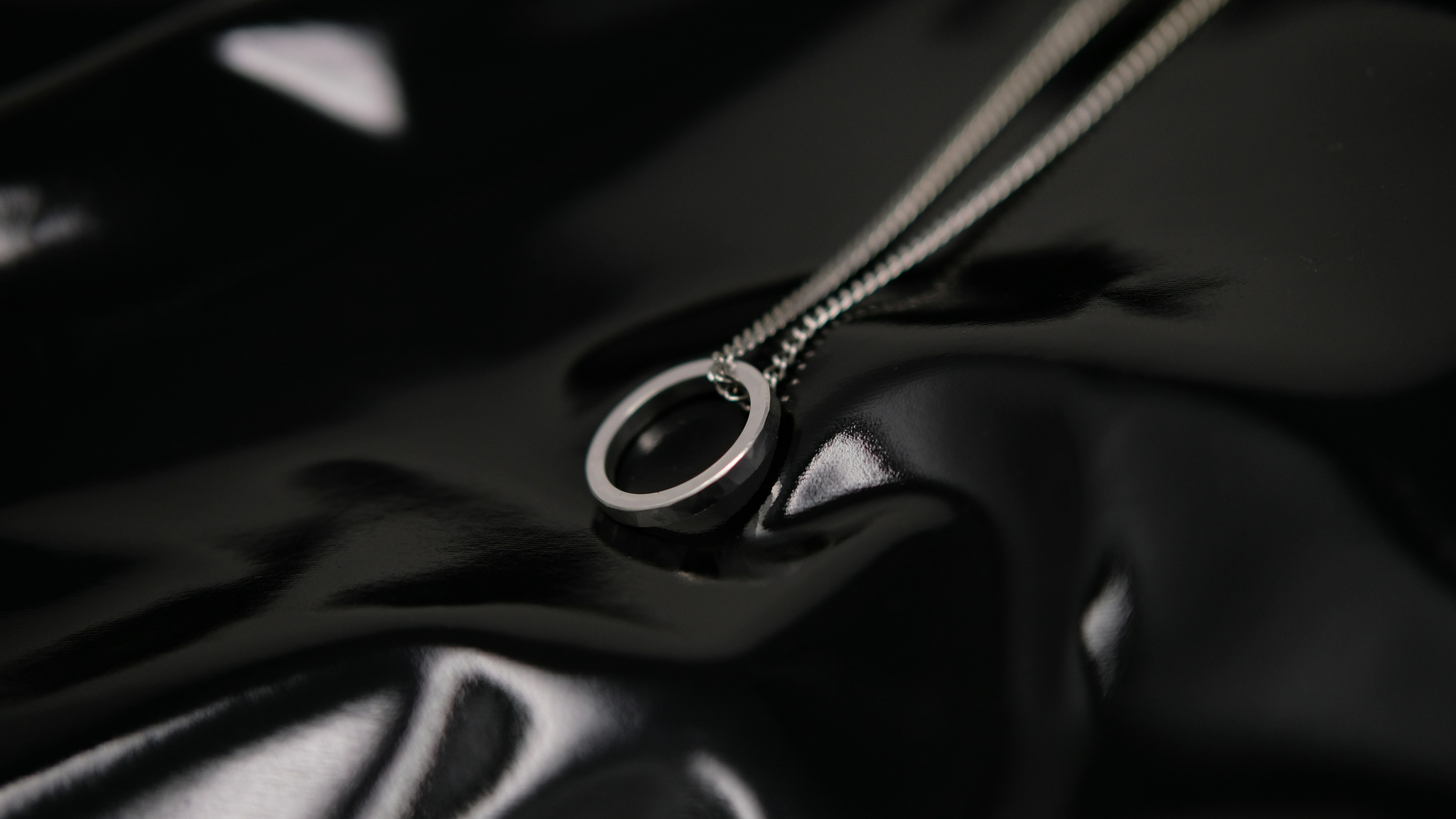 A silver ring pendant on a delicate chain against a glossy black surface