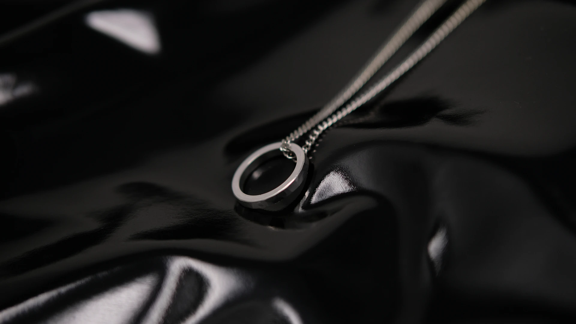A silver ring pendant on a delicate chain against a glossy black surface