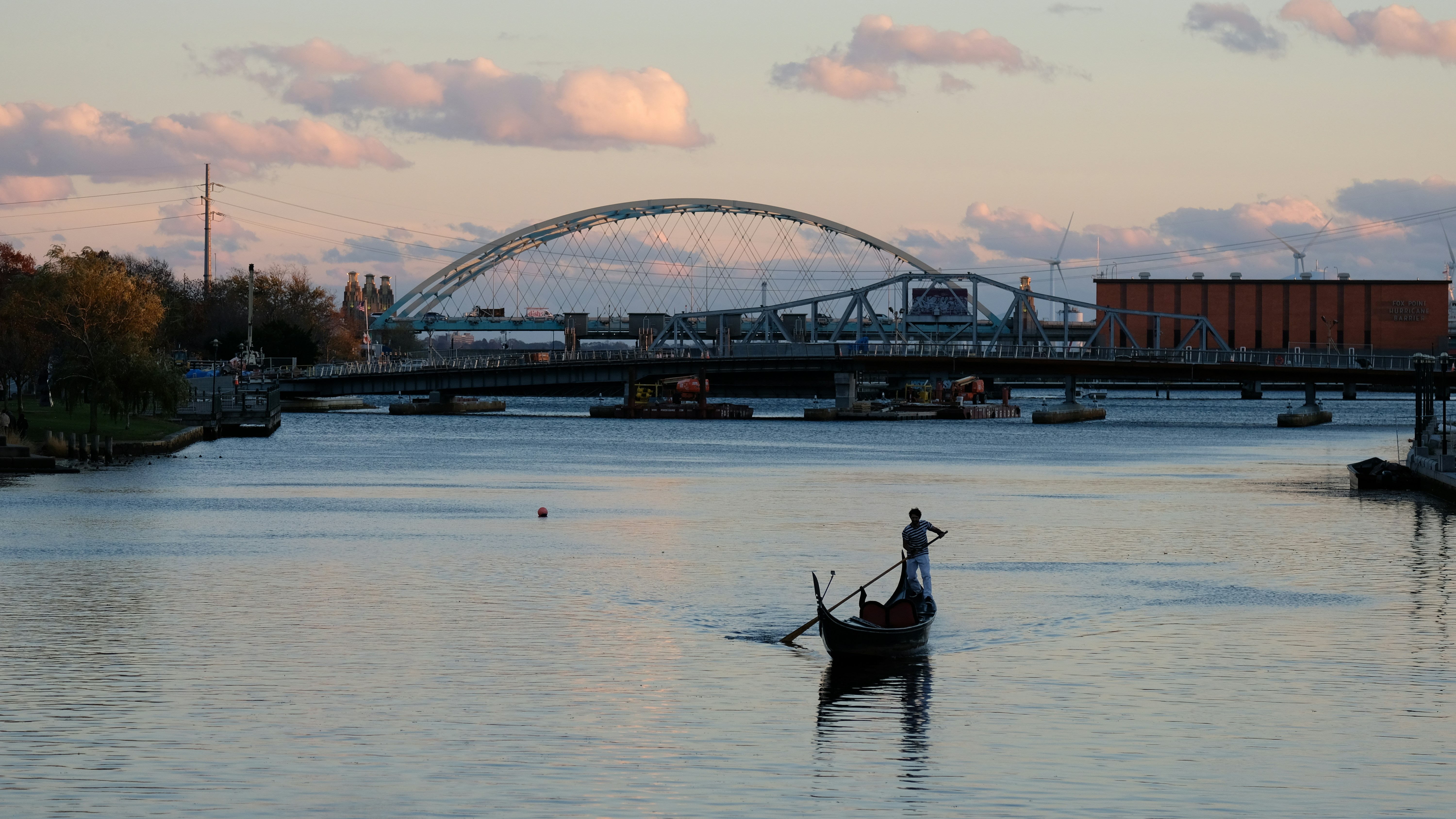 A person rowing a gondola on a river beneath a large arched bridge
